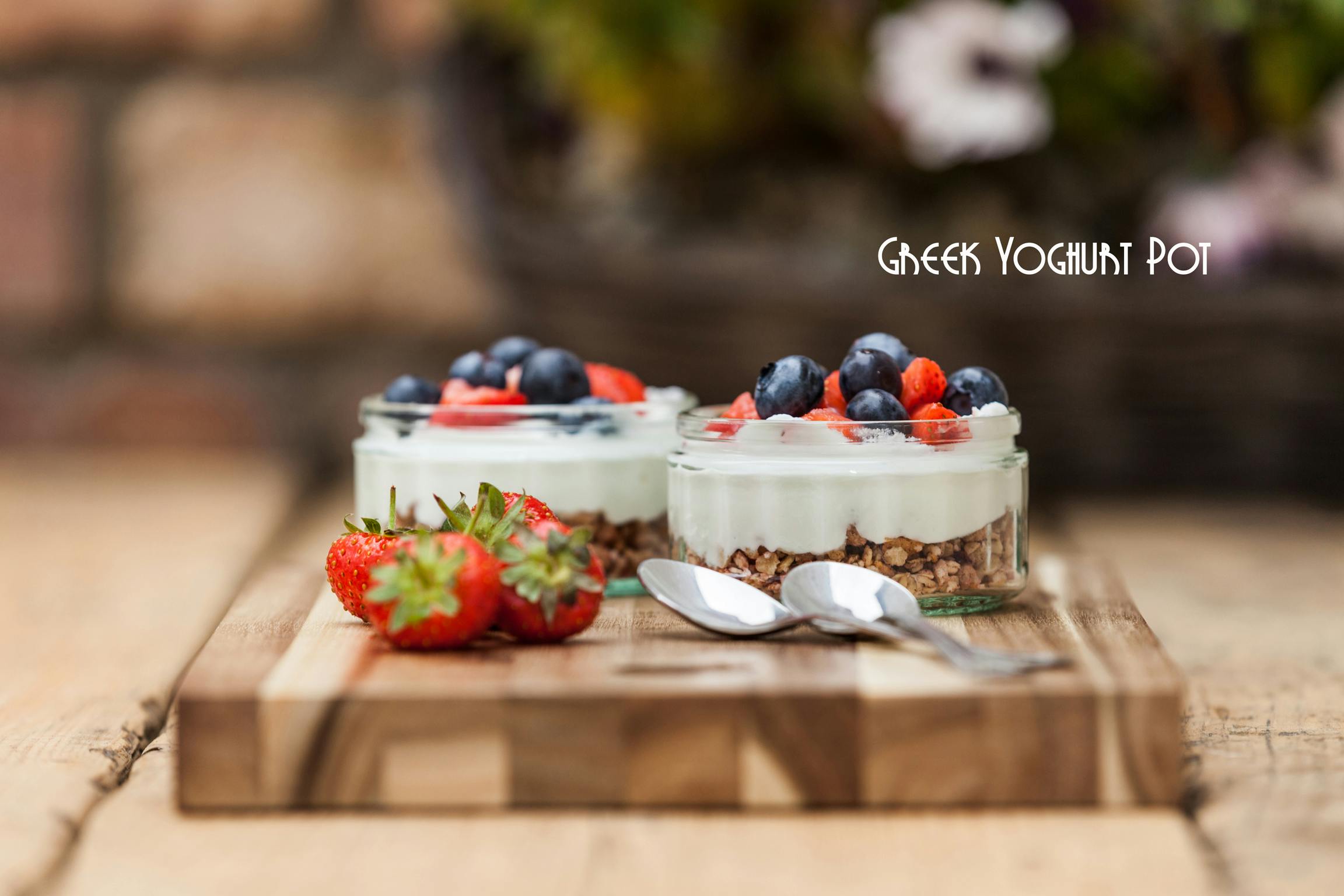 Two freshly prepared Greek yoghurt pots, with a mix of fresh fruits standing on a wooden board