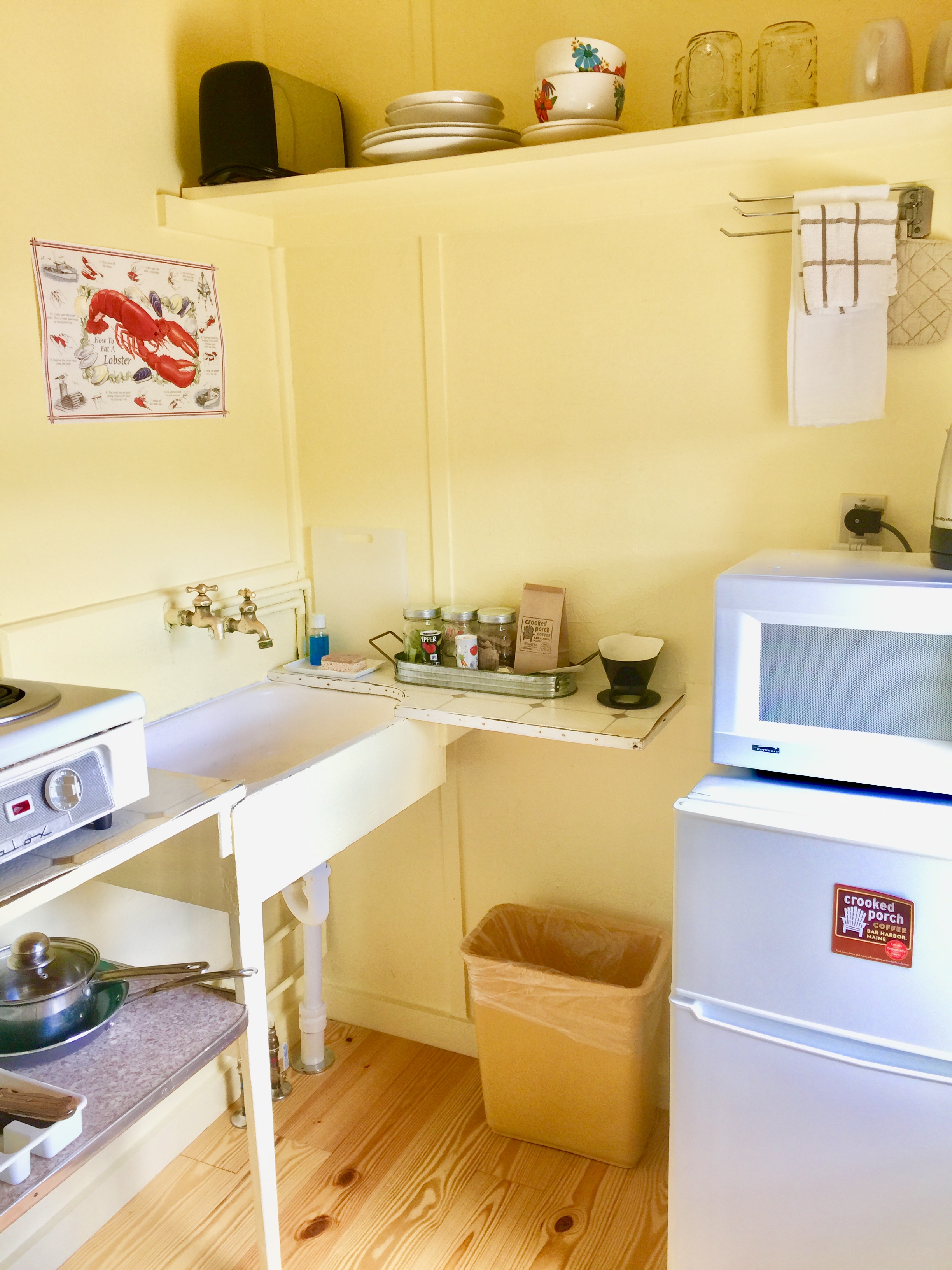 A small kitchen area with yellow walls, a sink, stove, microwave, and refrigerator.
