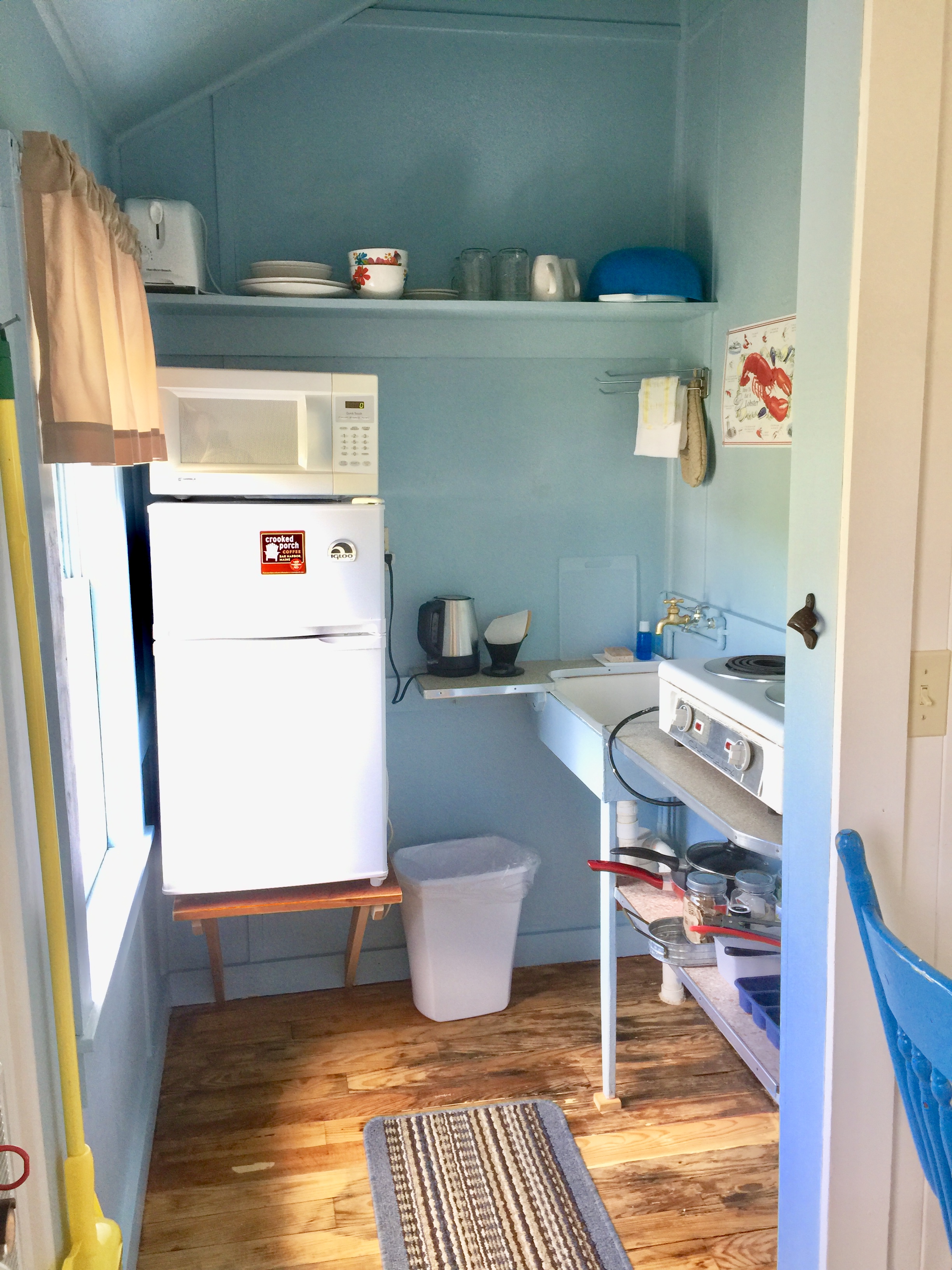 A small kitchenette with light blue walls, a white refrigerator, microwave, and stove.