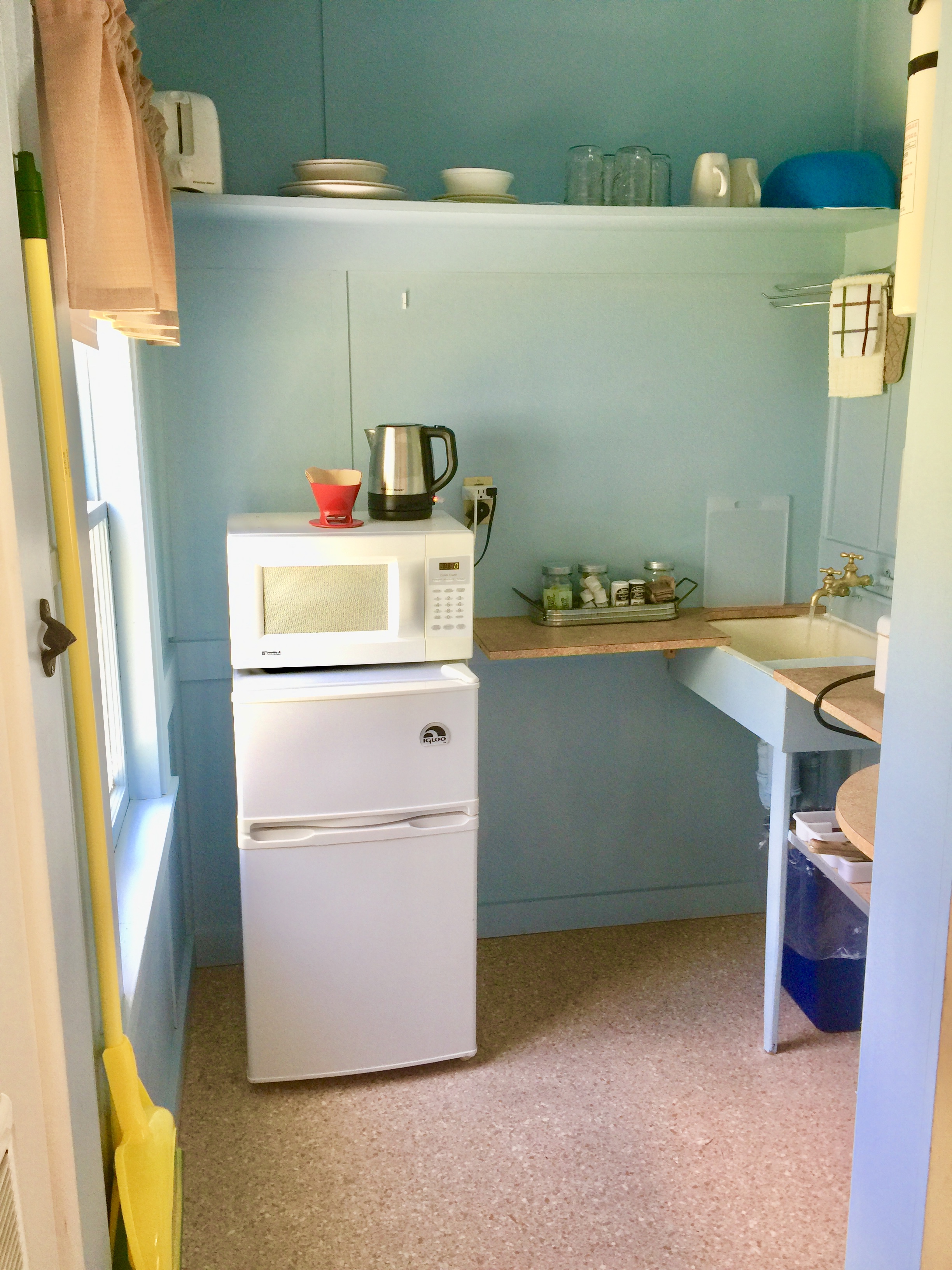 A small kitchenette with a microwave, refrigerator, sink, and shelf.