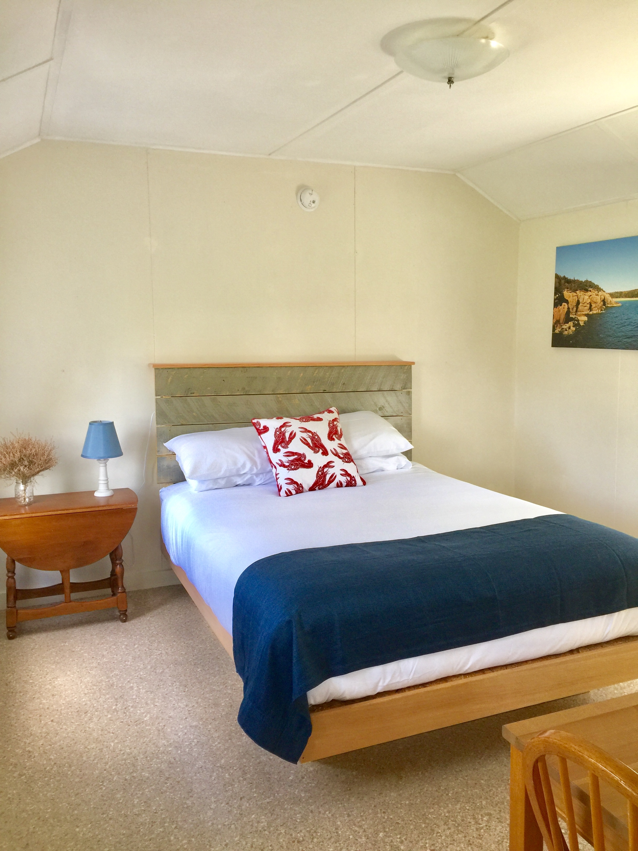 A neatly made bed in a room with a nightstand, lamp, and artwork.
