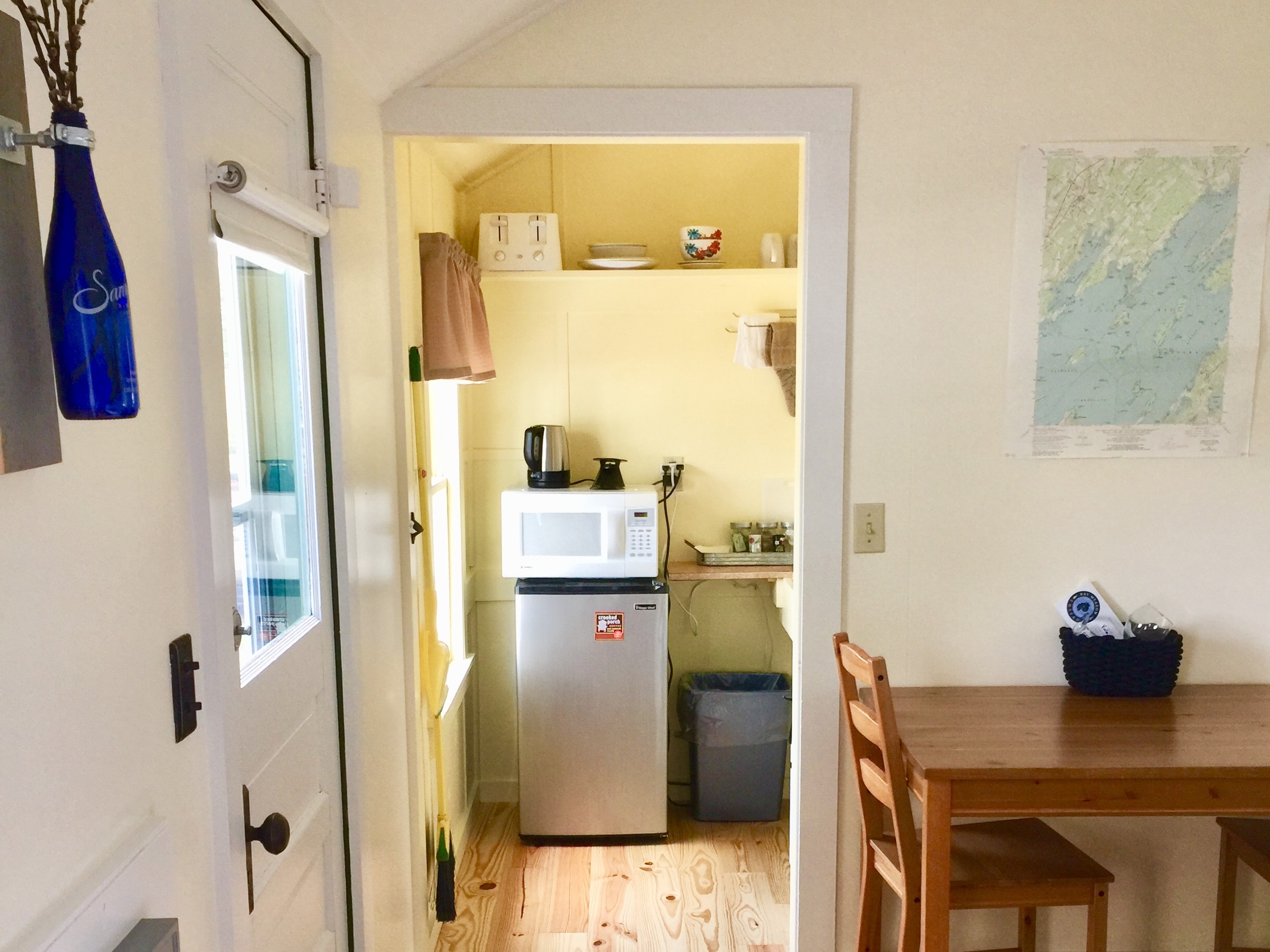 A small kitchenette with a microwave, refrigerator, and coffee maker, adjacent to a dining area with a table and chair.