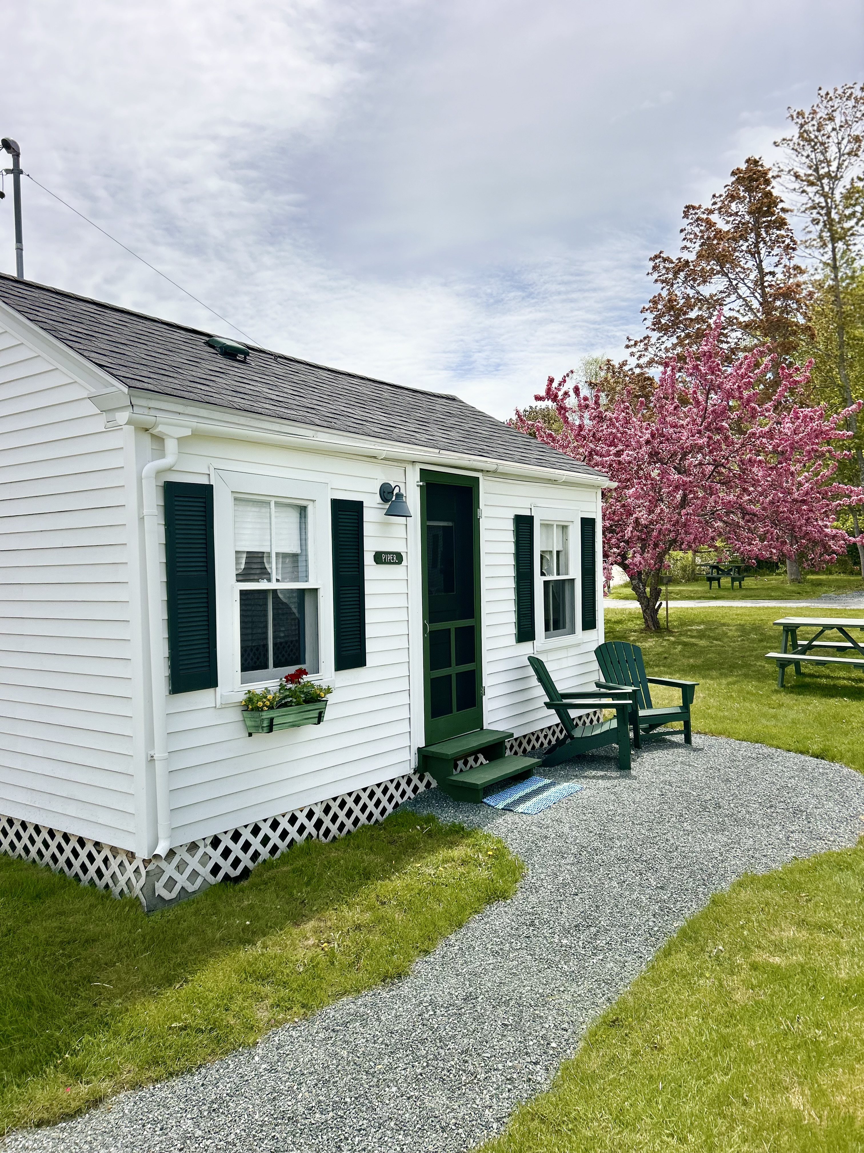 A small white cottage with green trim and a gravel pathway leading to the entrance