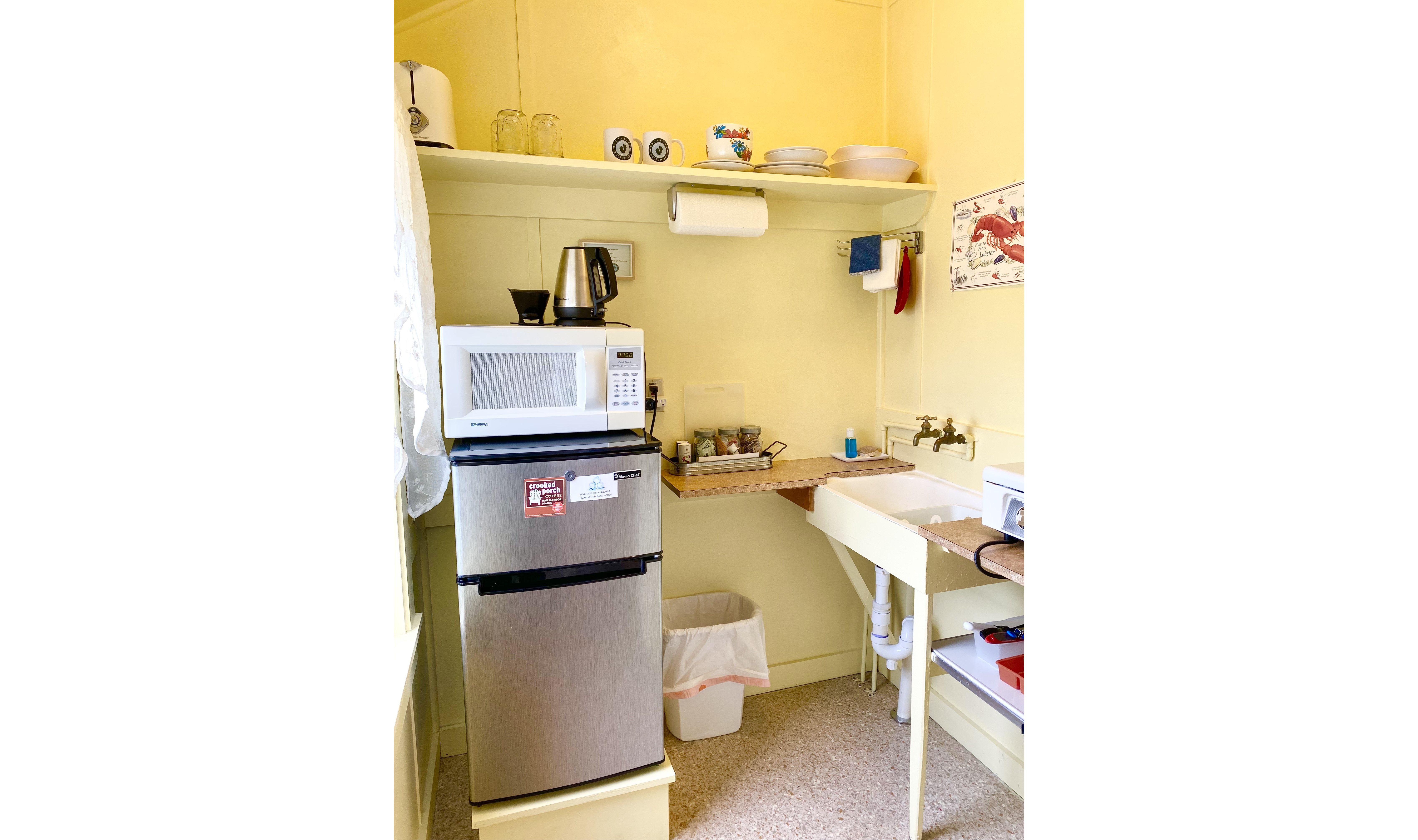 A small kitchenette with a refrigerator, microwave, sink, and shelf.