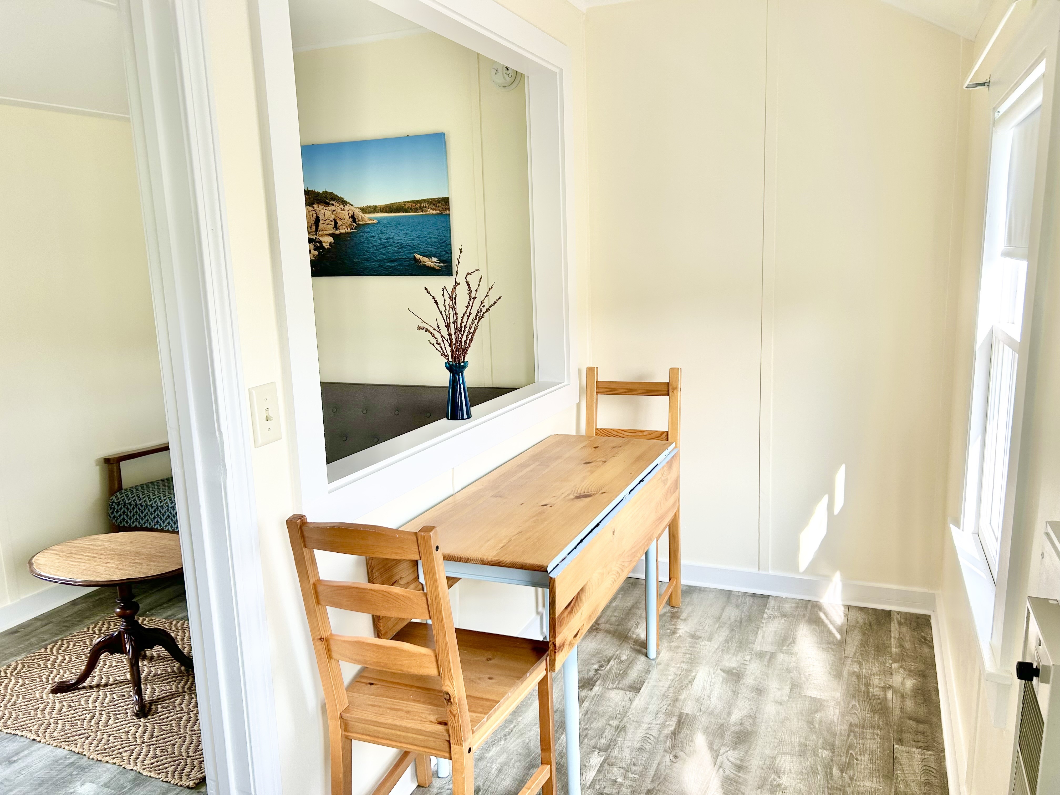 A room with a wooden desk and chairs, a window, and artwork on the wall.