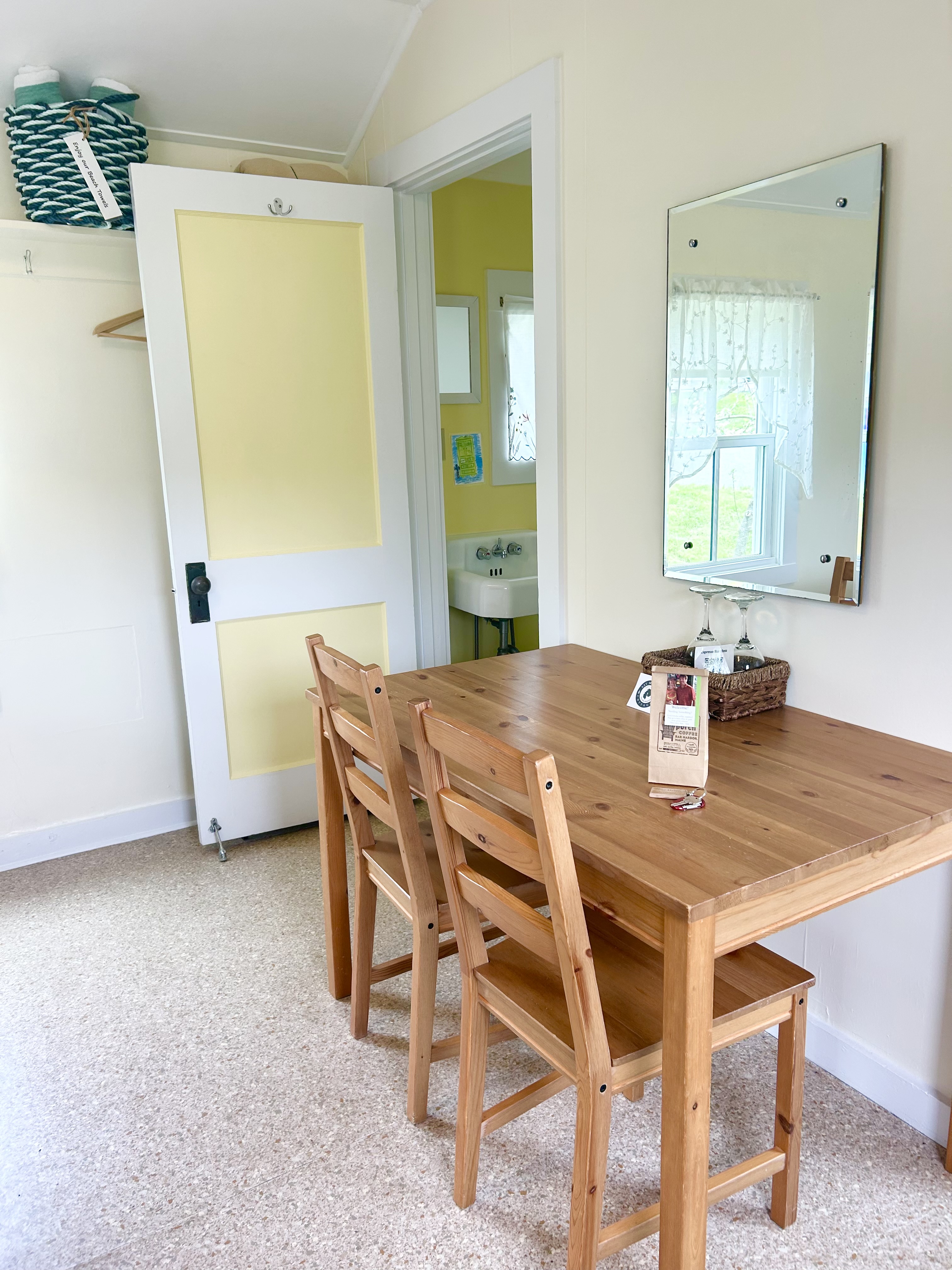 A dining area with a wooden table and chairs, a mirror on the wall, and a doorway leading to a bathroom.