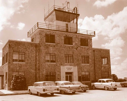 A stone building with a clock tower and vintage cars parked in front