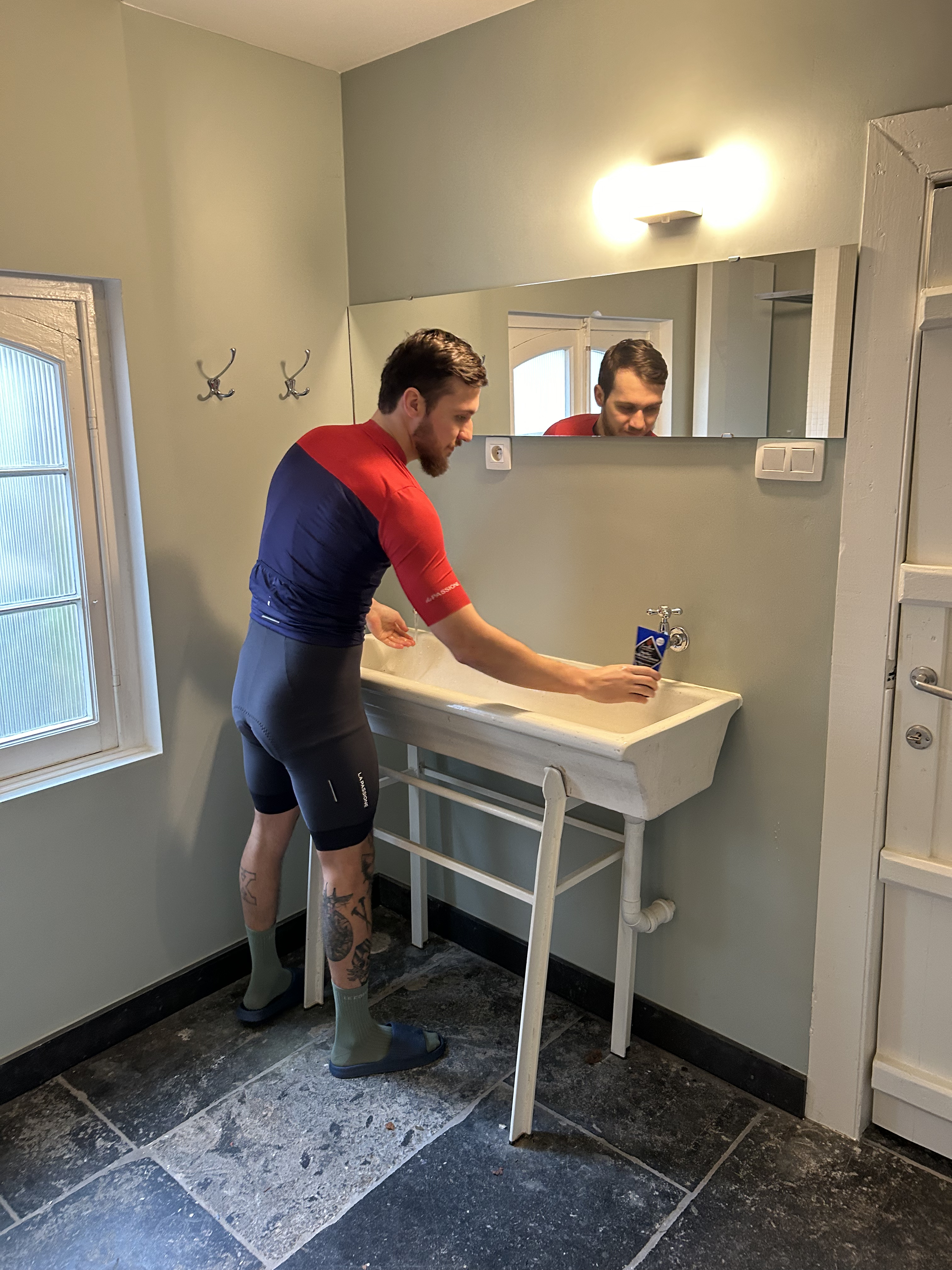 Cyclist washing their face at the sink in a shared, authentic bathroom with two showers at La Maison Vienvenue