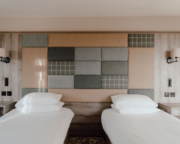 Twin beds in a hotel room with a tweed and leather fabric covered accent wall.