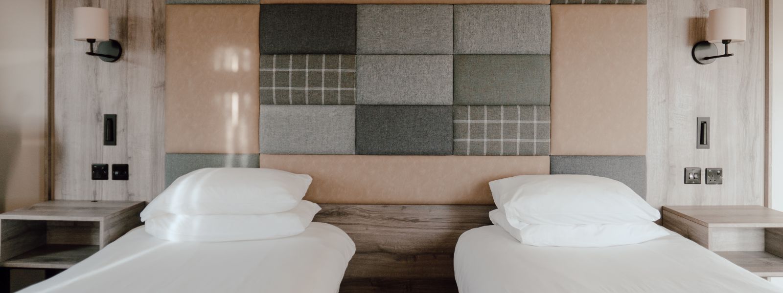 Twin bedroom with a tweed and leather fabric covered accent wall and white linen.