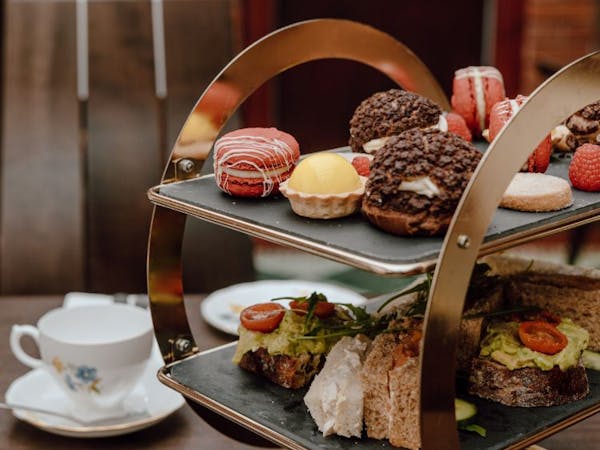 A table displaying an afternoon tea tray of pastries, including scone, macaron, lemon tart and sandwich.