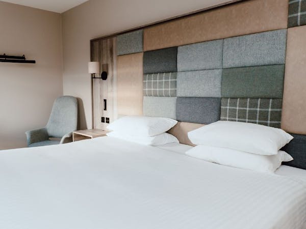 Double bed in a hotel room with a tweed and leather fabric covered accent wall.