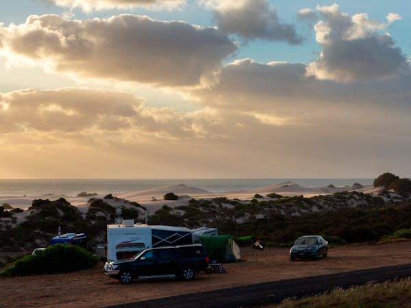 "Un-Powered-caravan-and-camping-with-caravans-tents-and-cars-in-the-foreground-with-view-of sanddunes-&-ocean-in-background"