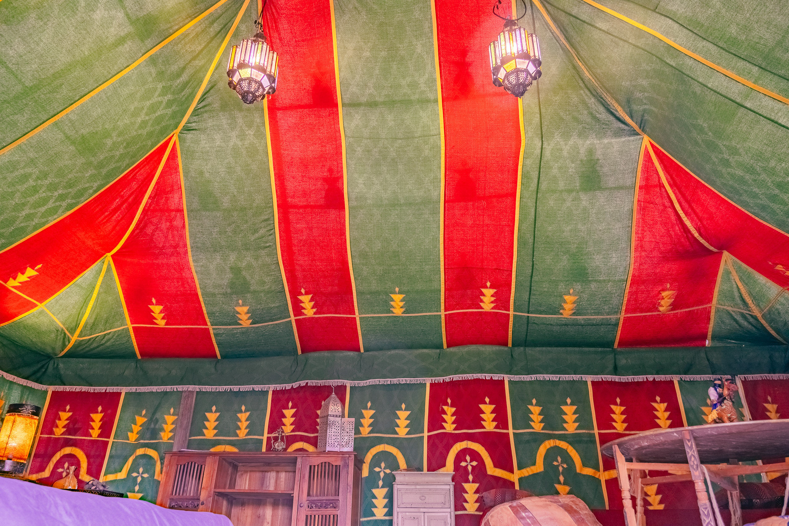 Au-Bonheur-Nomade - vue intérieure de la tente caïdale Marocaine. Plan sur la toile doré rouge et verte et les luminaires