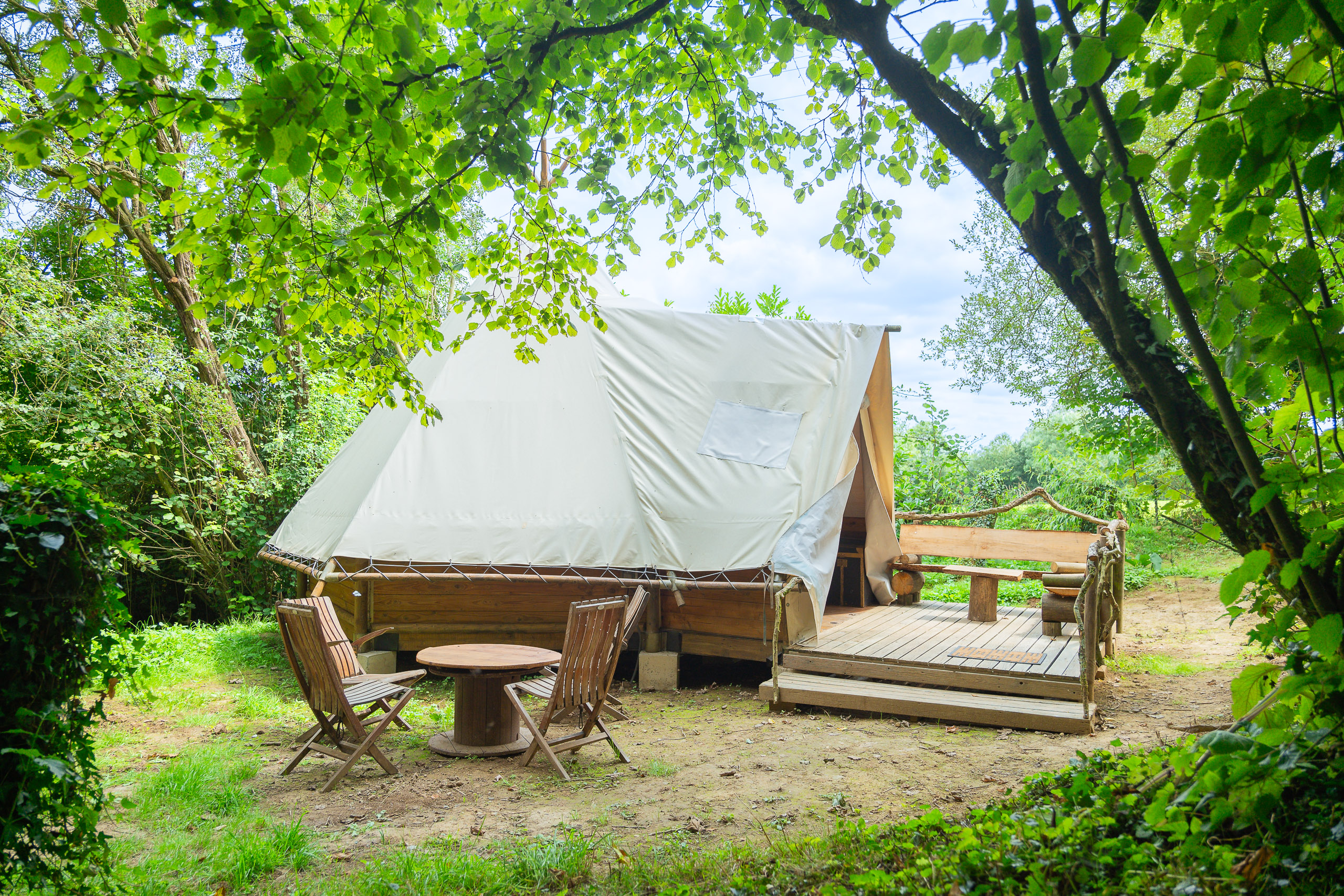 Au-Bonheur-Nomade - vue extérieure du tipi trappeur, à travers les arbres, mobilier d'été