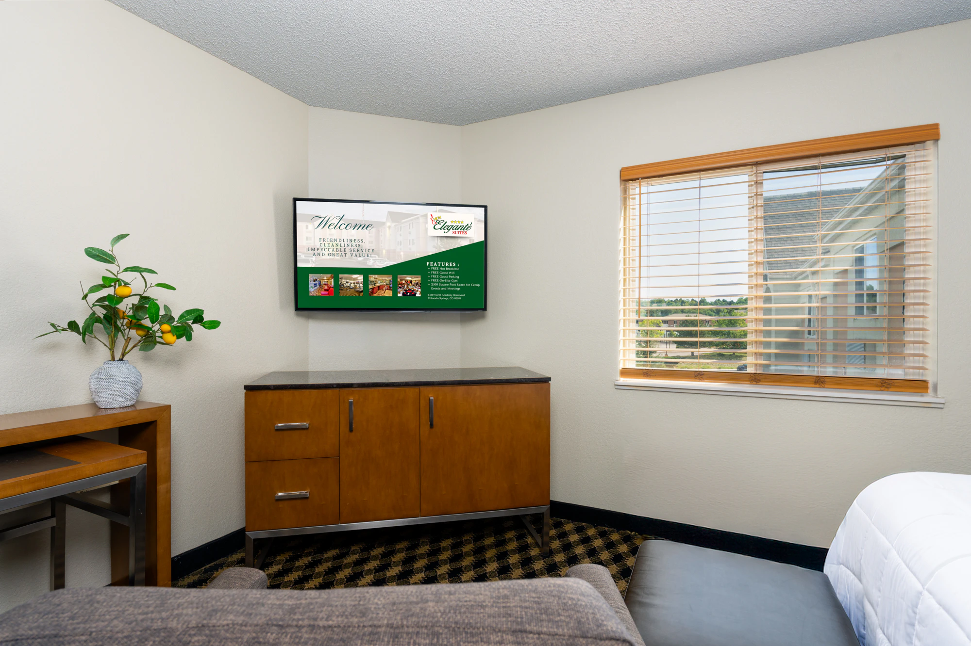 A hotel room with a TV, desk, window, and bed.