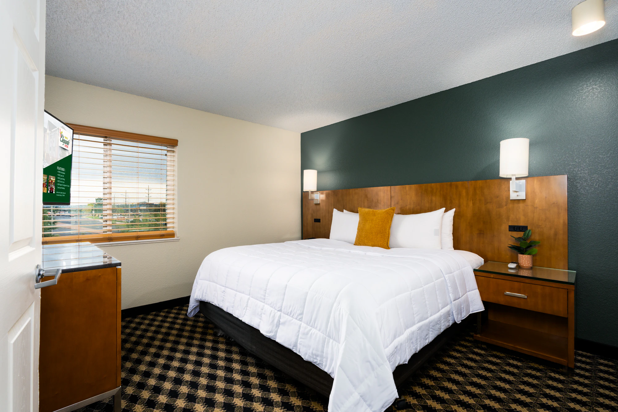 A hotel room with a king-sized bed, nightstand, and window.