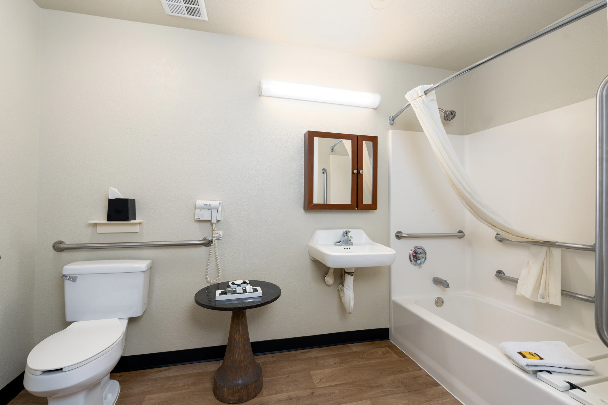 A clean and well-organized bathroom with a toilet, sink, bathtub, and grab bars.