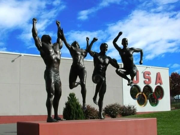 A statue of four athletes in front of a building with the Olympic rings and 'USA' sign.