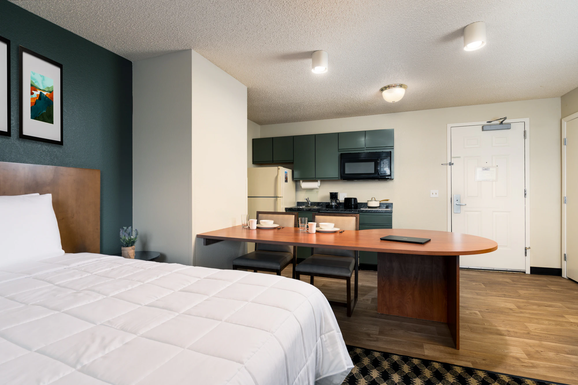 A hotel suite with a kitchenette, dining table, and bed