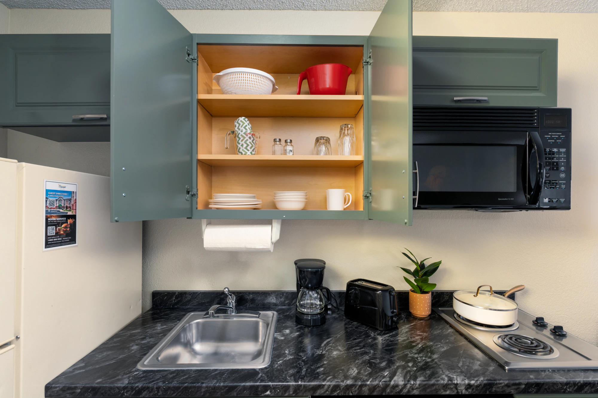A small kitchenette with a sink, microwave, stove, coffee maker, and toaster.