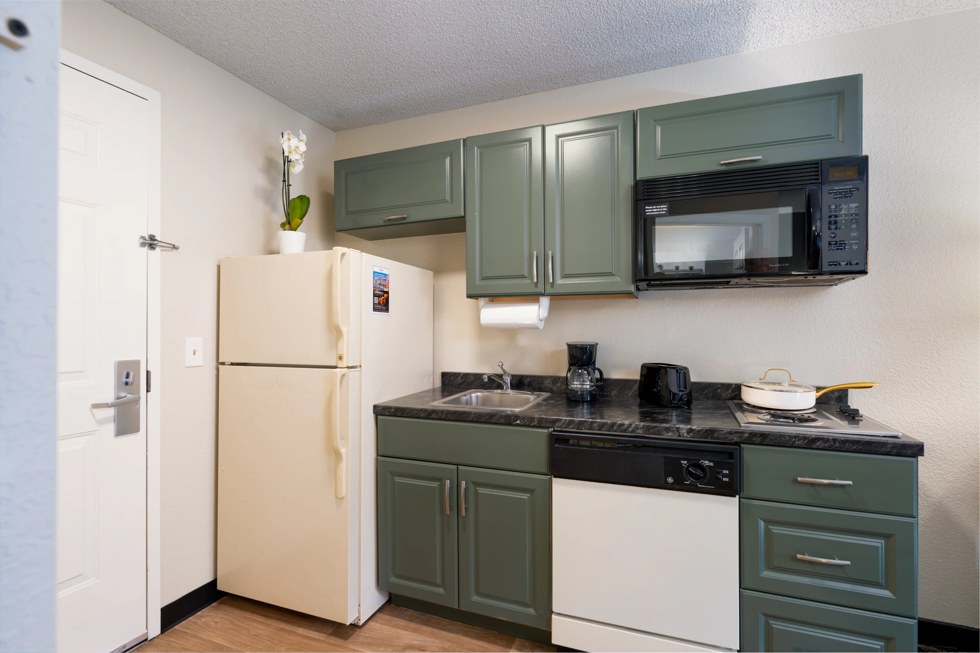 A compact kitchenette with green cabinets, black countertops, and white appliances.