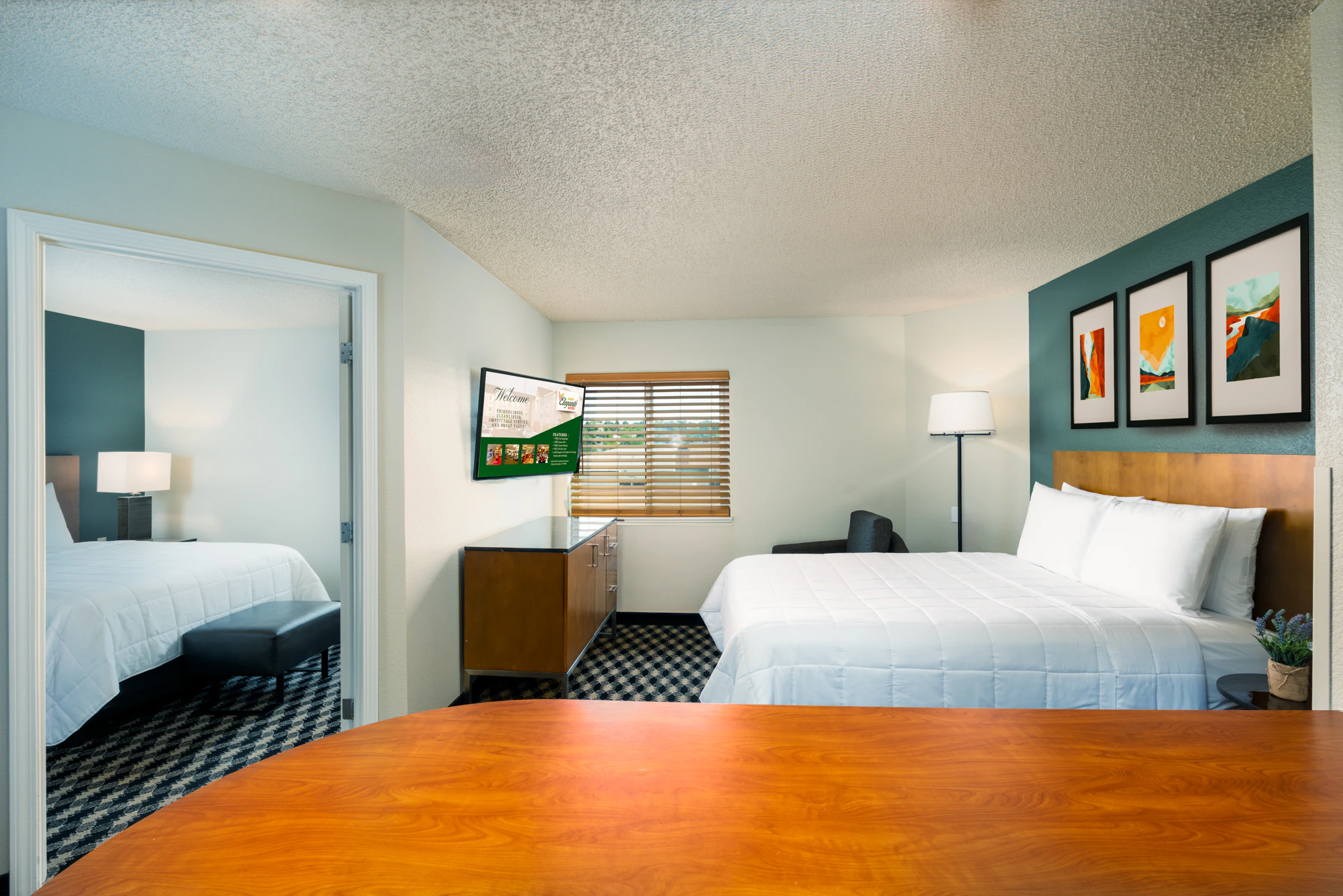 A hotel room with a large bed, desk, TV, and artwork.