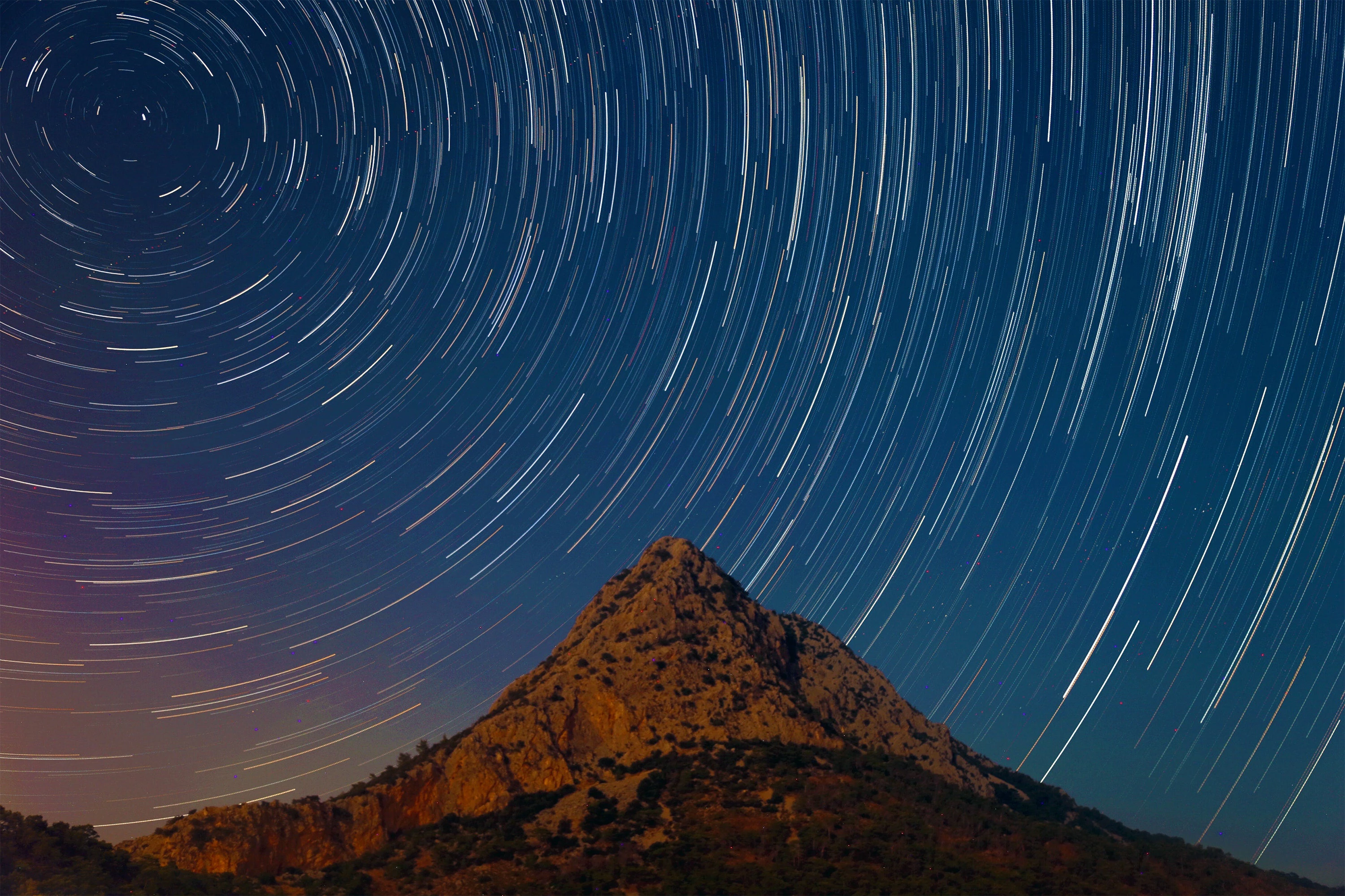 a mountain under a starry night sky with star trails