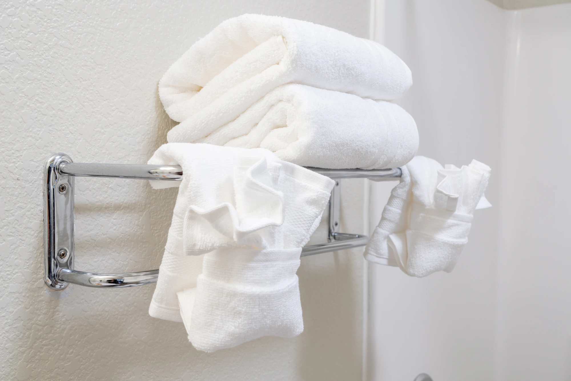 A stack of white towels on a silver towel rack in a bathroom.