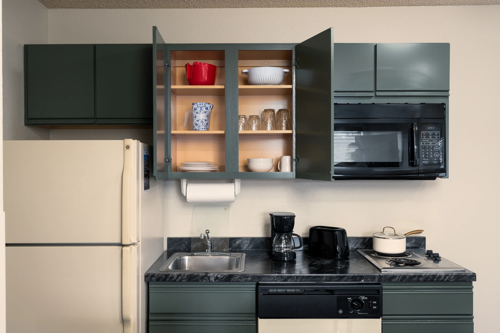 A compact kitchenette with green cabinets, black countertop, and essential appliances.