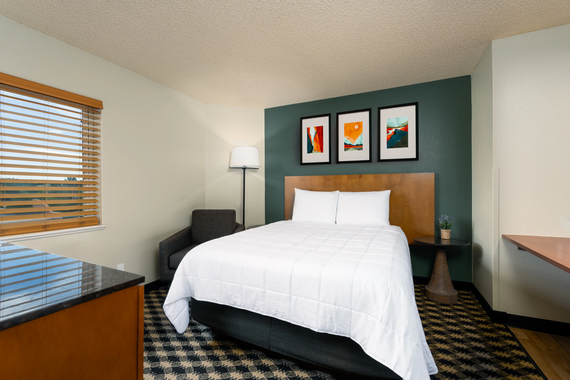 A hotel room with a large bed, chair, lamp, and artwork on the wall.