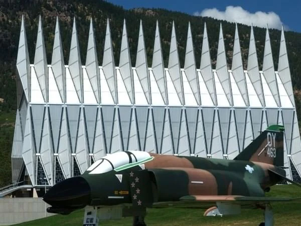 A military jet on display in front of a large white building with a unique architectural design.