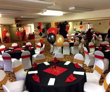 a banquet hall with round tables and chairs, decorated with red, black, and gold balloons and tablecloths
