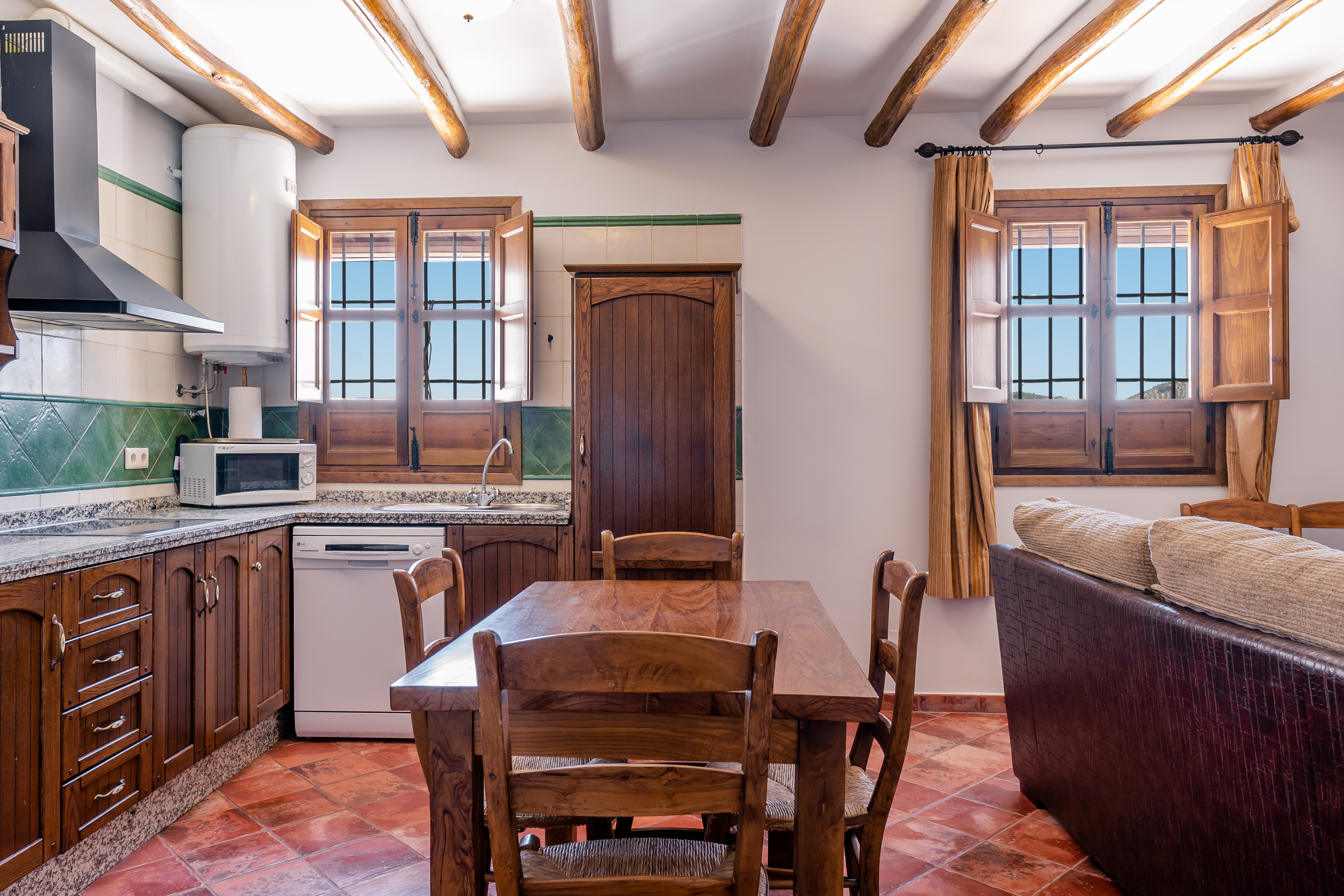 Interior of a holiday apartment showing living area with wooden ceiling beams and tiled floor