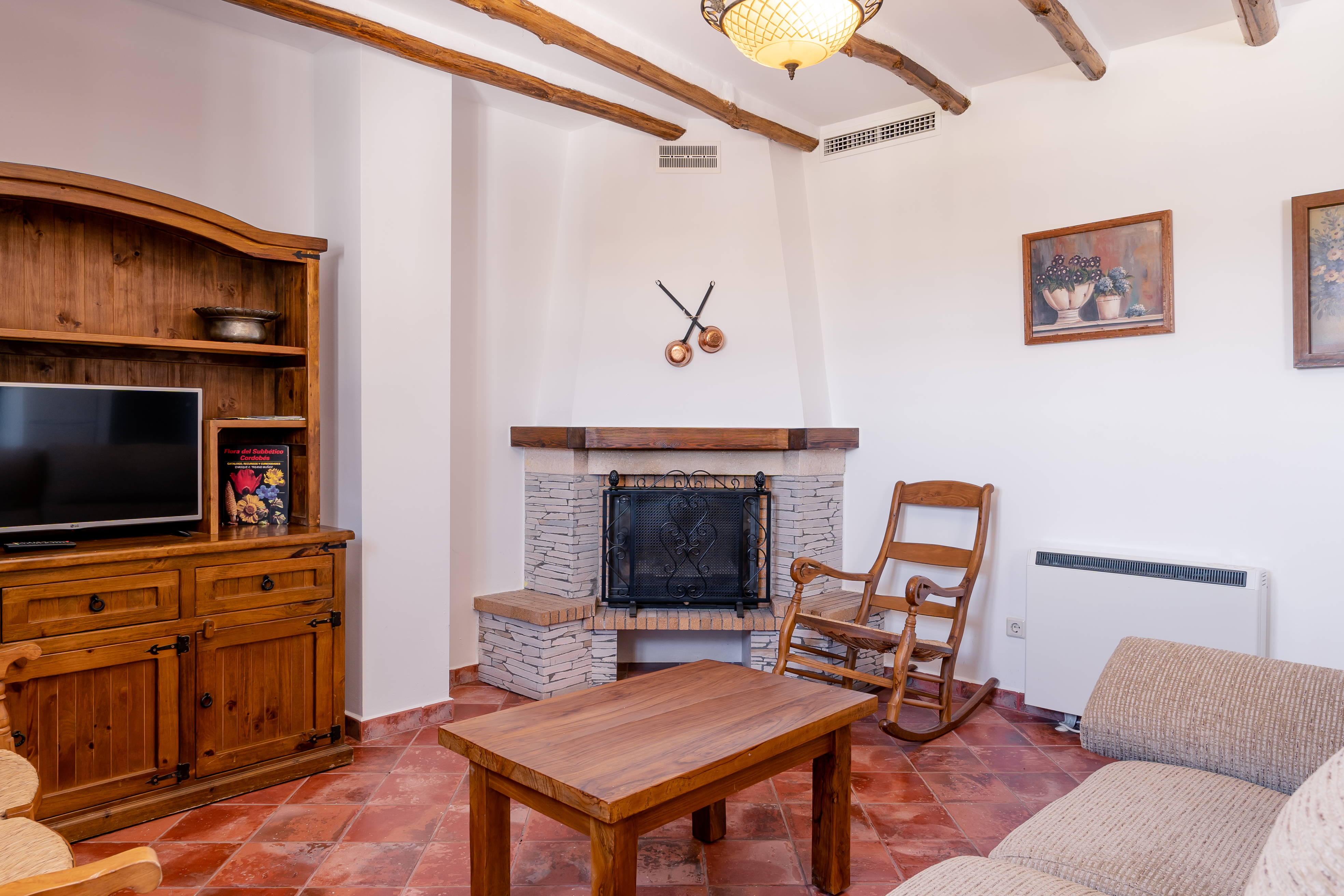 Interior of a holiday apartment showing living area with wooden ceiling beams and tiled floor