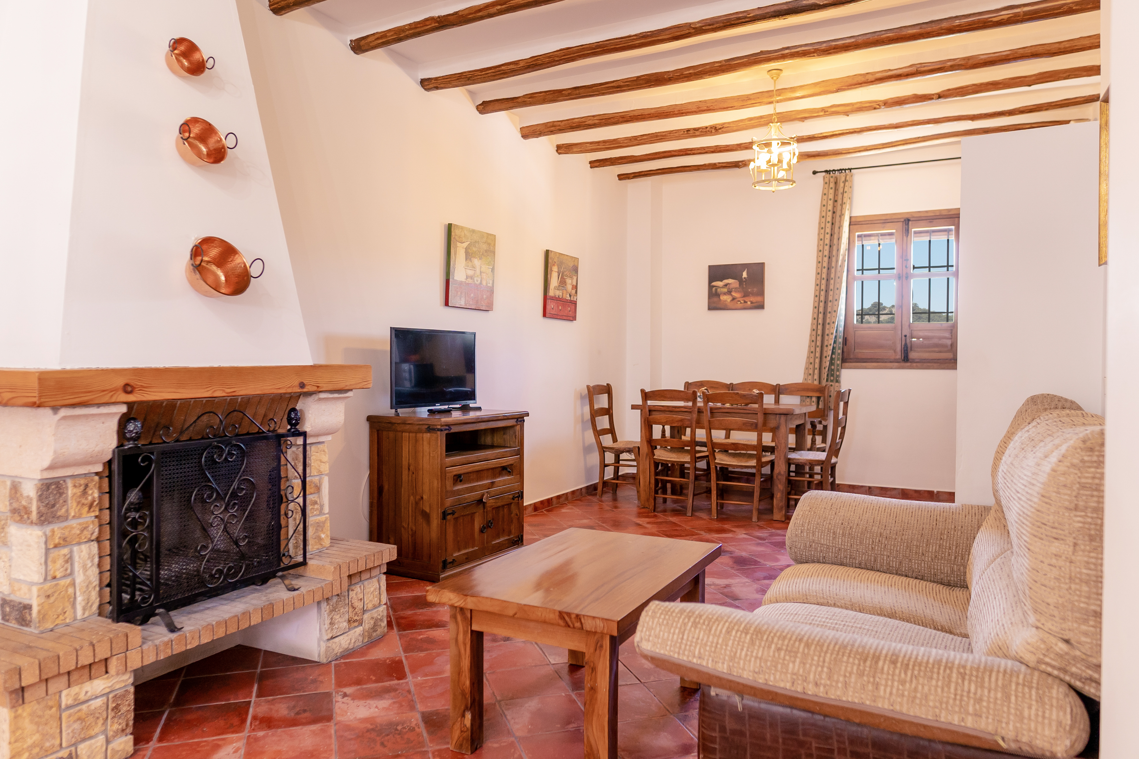 Interior of a holiday apartment showing living area with wooden ceiling beams and tiled floor