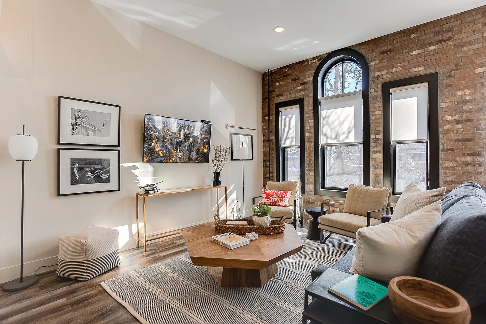 A wide view of a living room with a brick wall, large windows, and modern furniture.