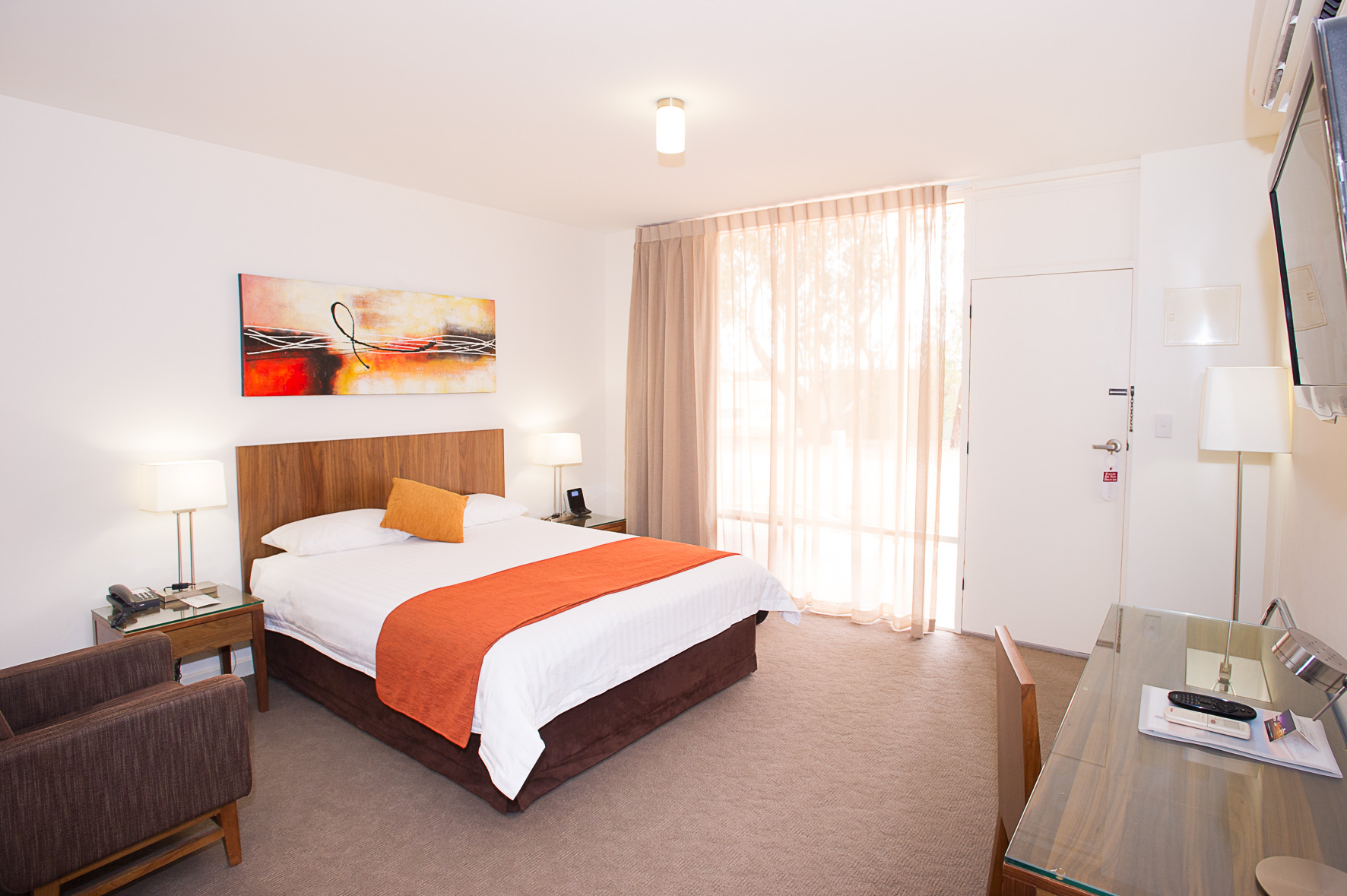 Modern hotel room with king bed, desk, and armchair.