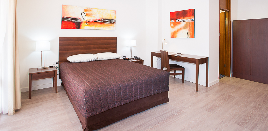 Modern room with queen bed, desk, artwork, and ample natural light.