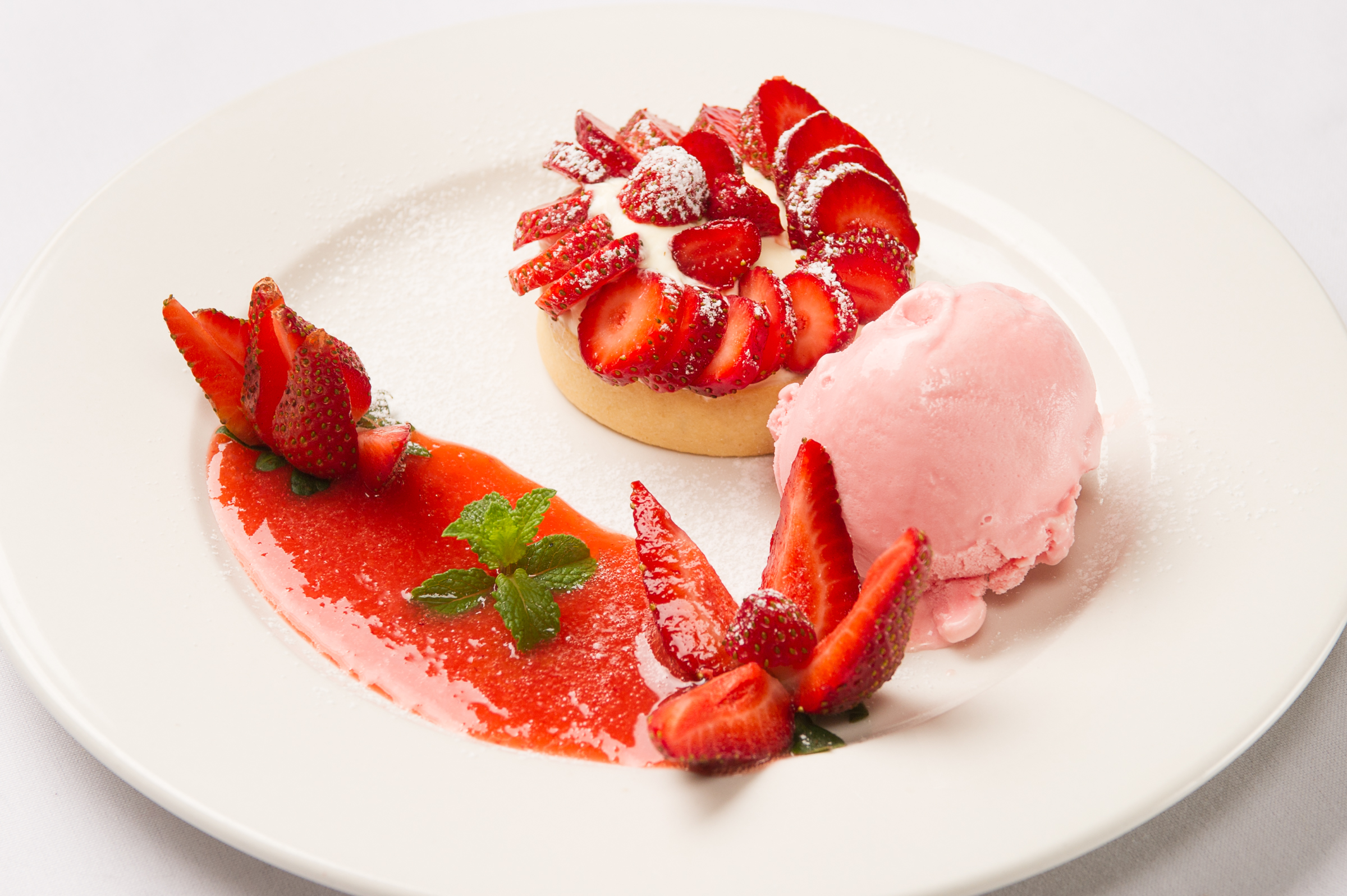Indulgent strawberry dessert: tartlet with fresh berries, sauce, and creamy ice cream.