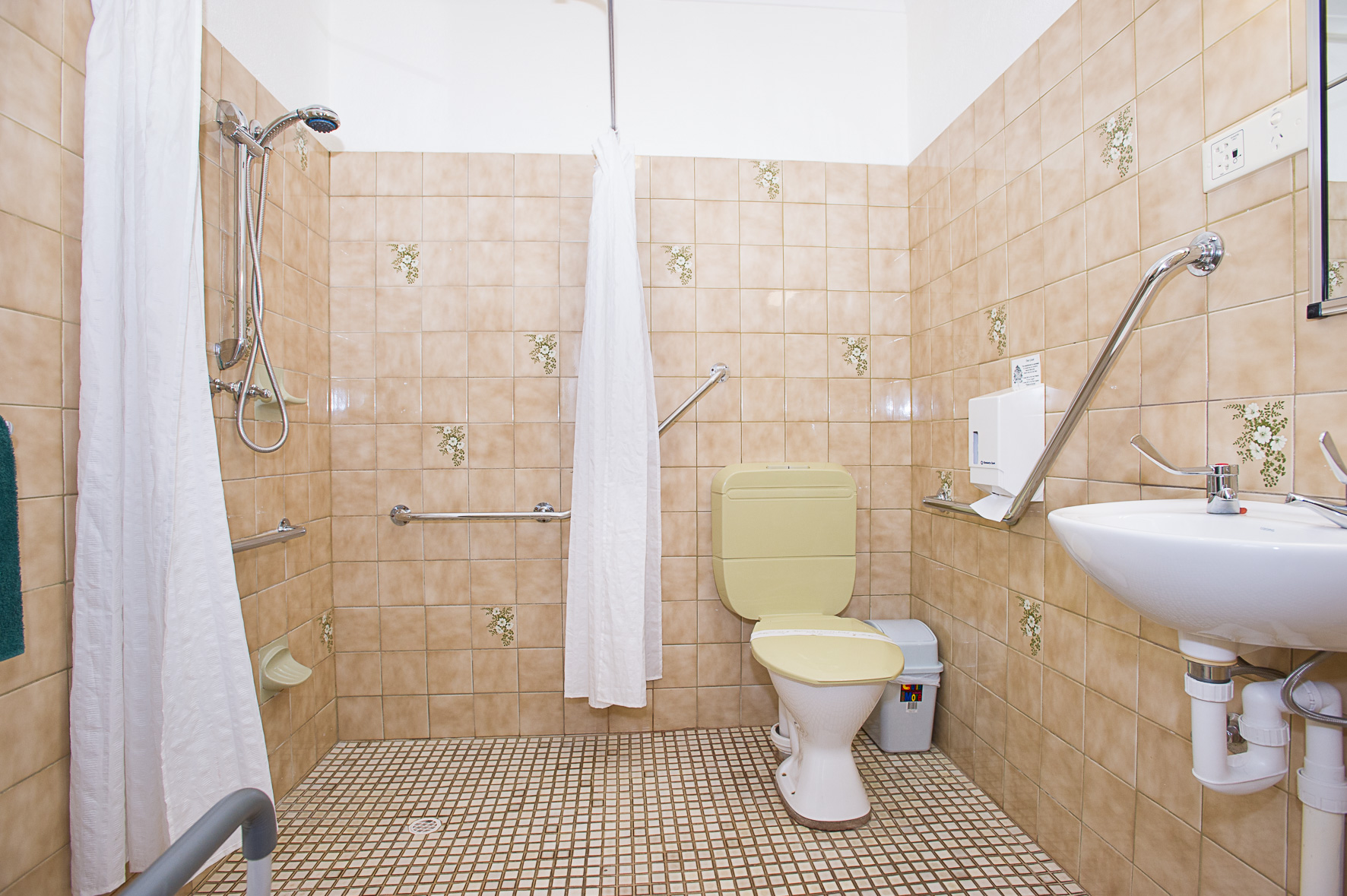 Light-colored bathroom featuring shower, commode, and hand grips.