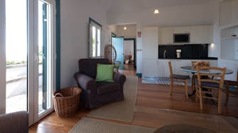 Kitchen dining area in cottage suite, wooden floors, wicker basket, comfortable chair, windows to vineyard Quinta das Vinhas
