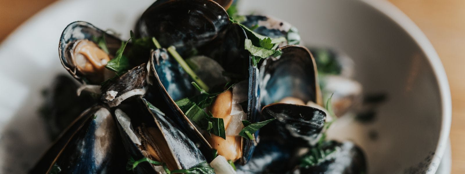 A bowl of mussels with fresh herbs on a wooden table, showcasing a delectable seafood dish.
