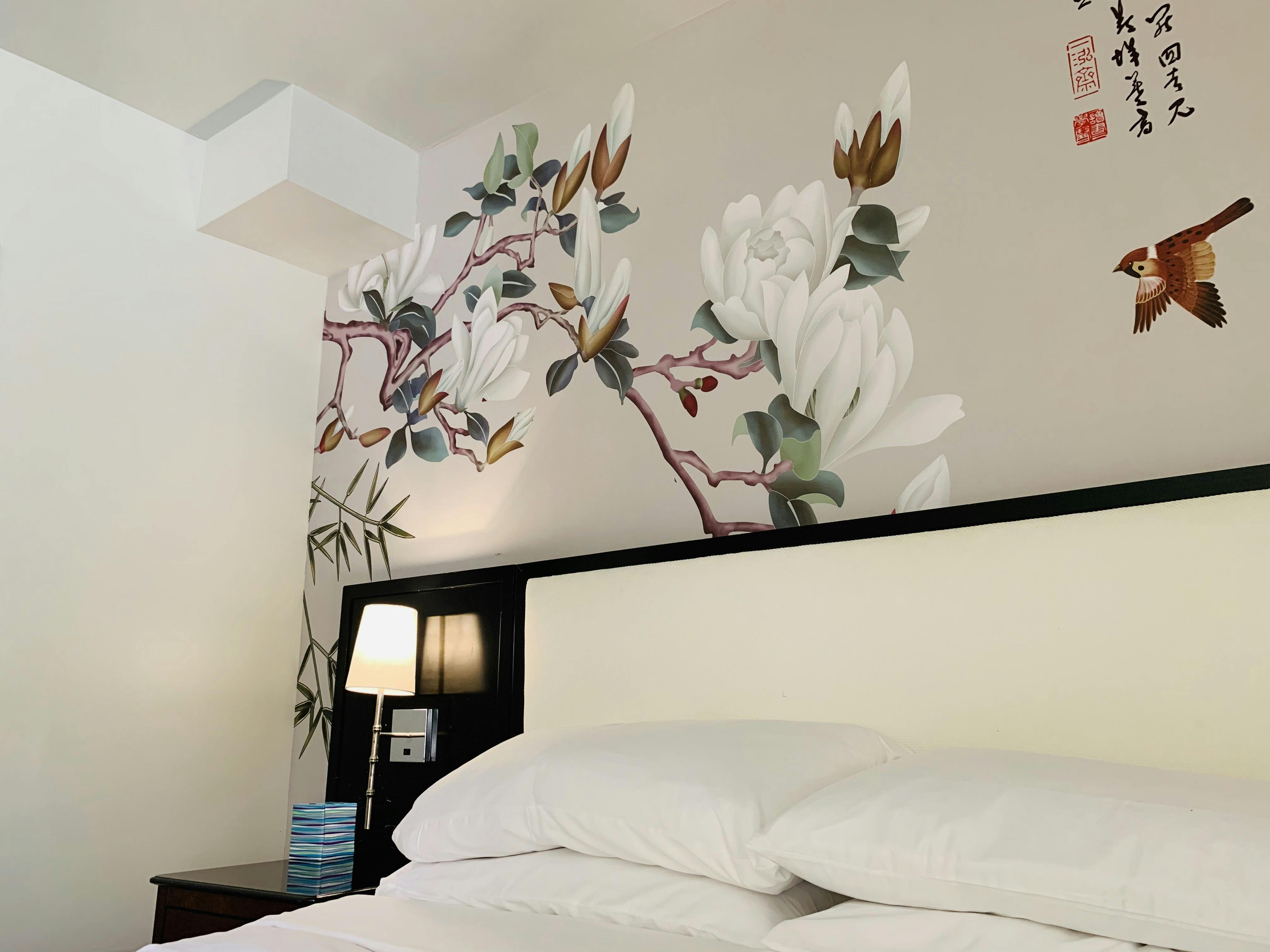 Art wall in WangShi Palace guest room — elegant Chinese floral painting with a warm bedside setting.