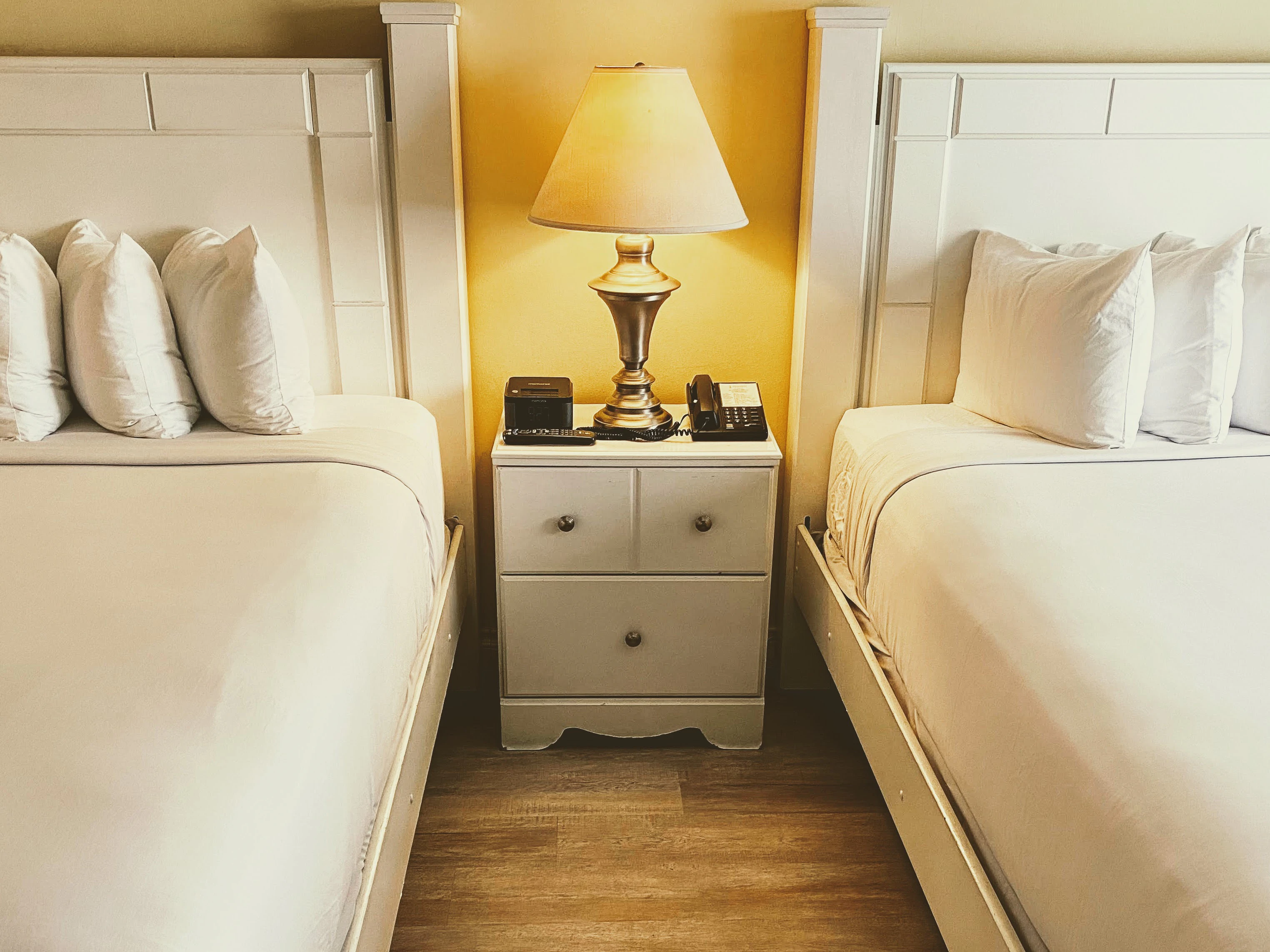 A hotel room with two white beds and a nightstand with a lamp.
