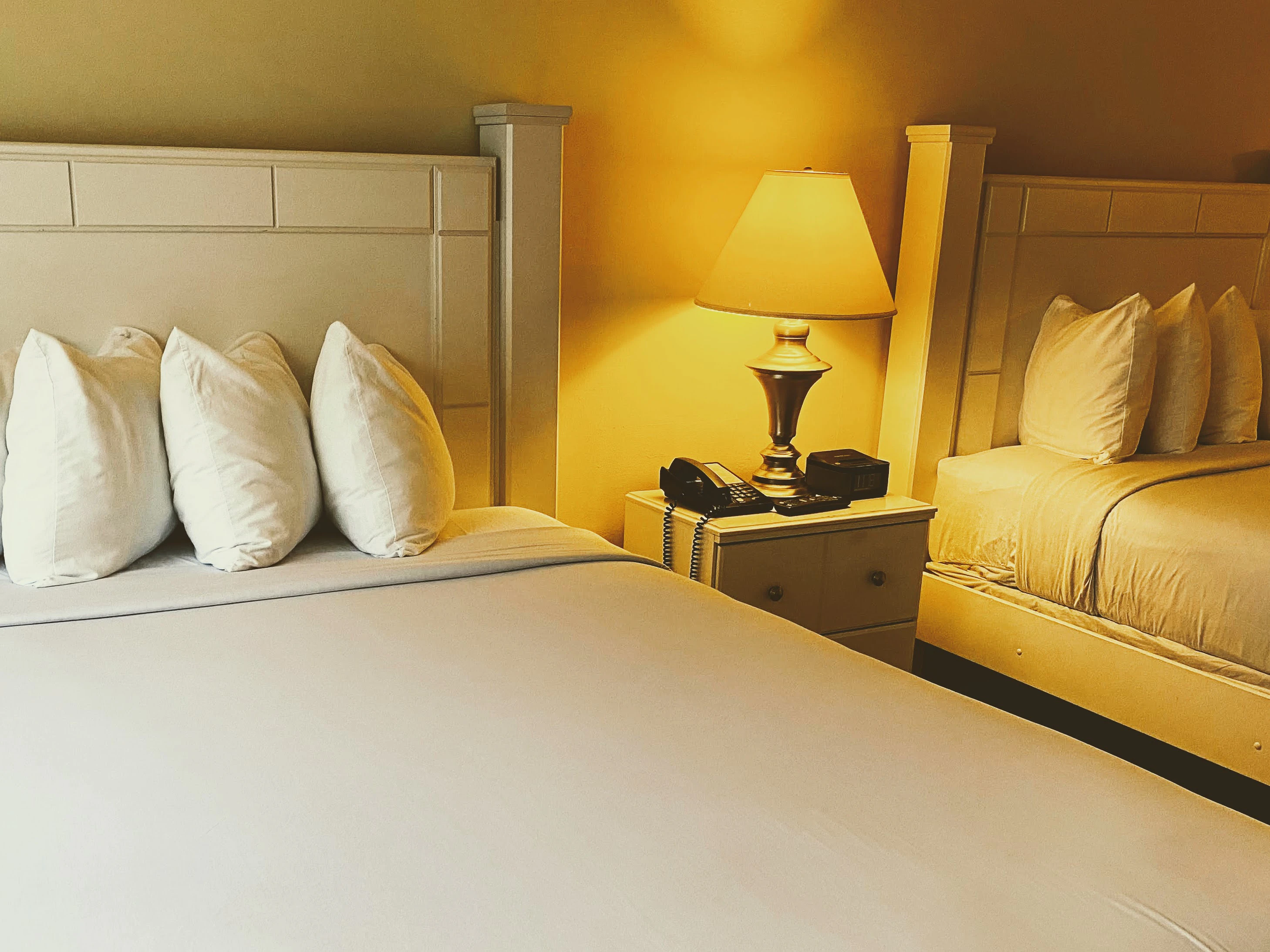 A hotel room with two twin beds, white bedding, and cream-colored furniture.