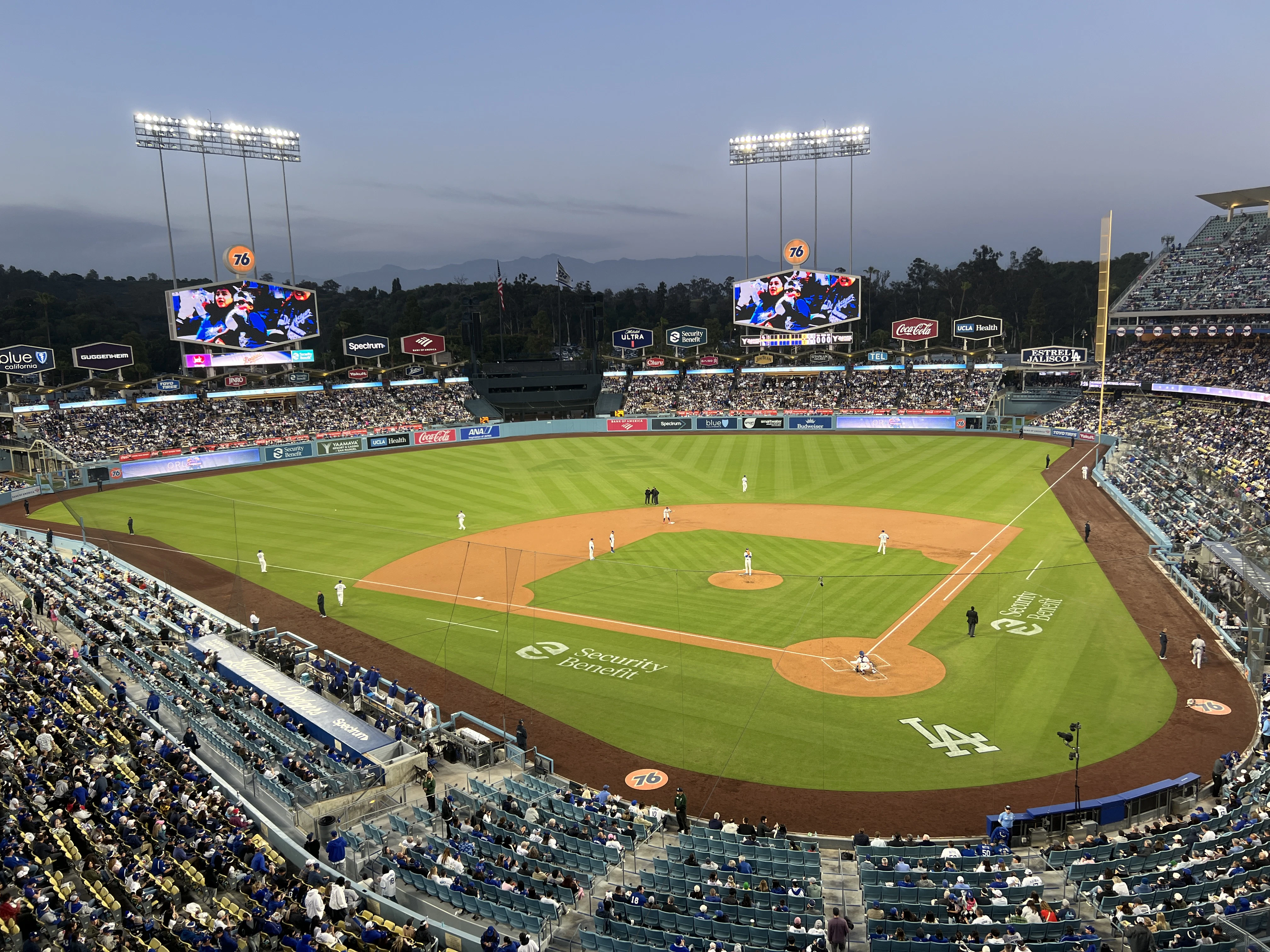 A baseball stadium with a green field and brown dirt, surrounded by seating and advertisements, under a clear blue sky.