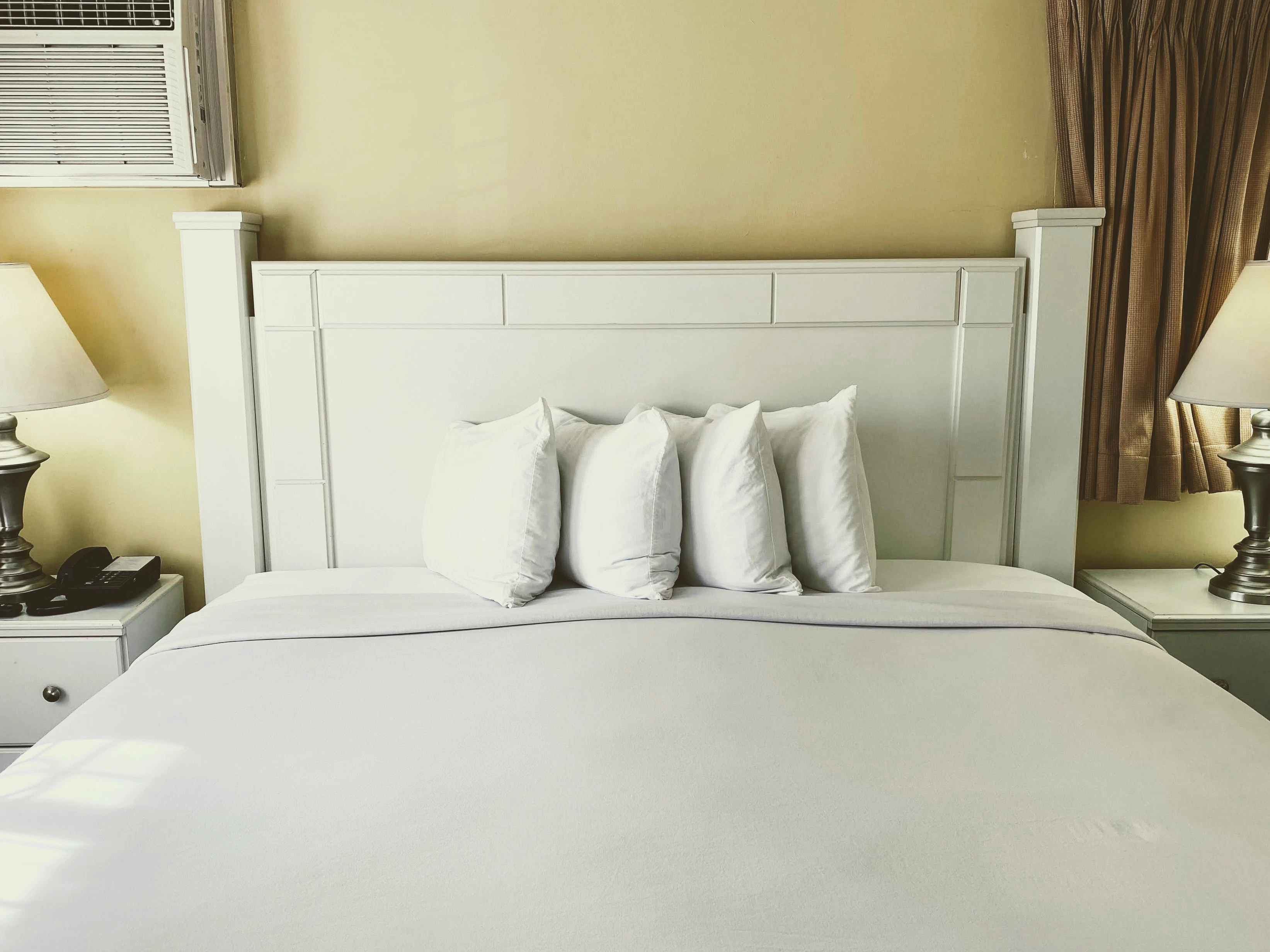 A neatly made bed with white linens and pillows, flanked by two nightstands with lamps.