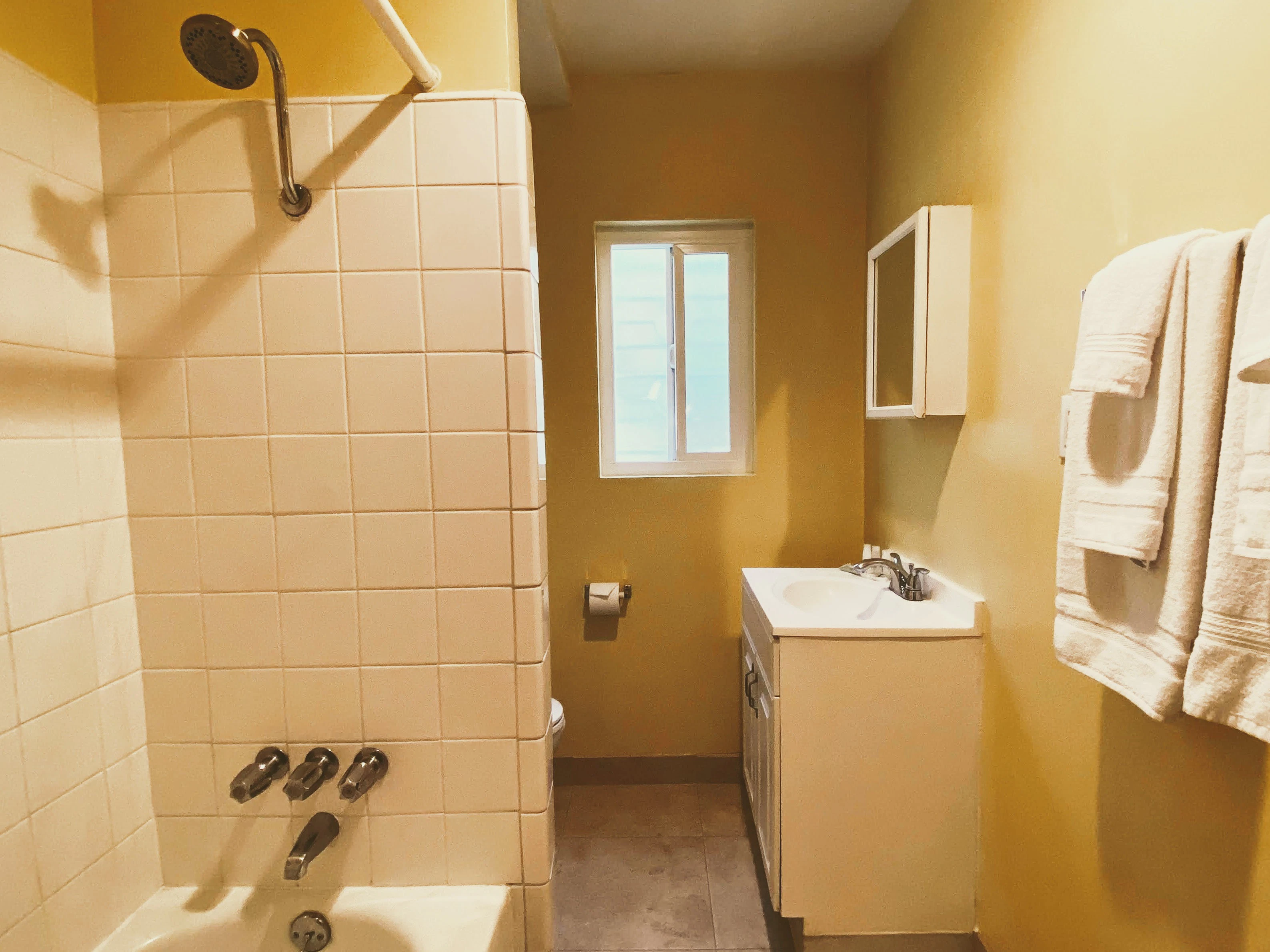 A bathroom with a tiled shower, sink, and towels.