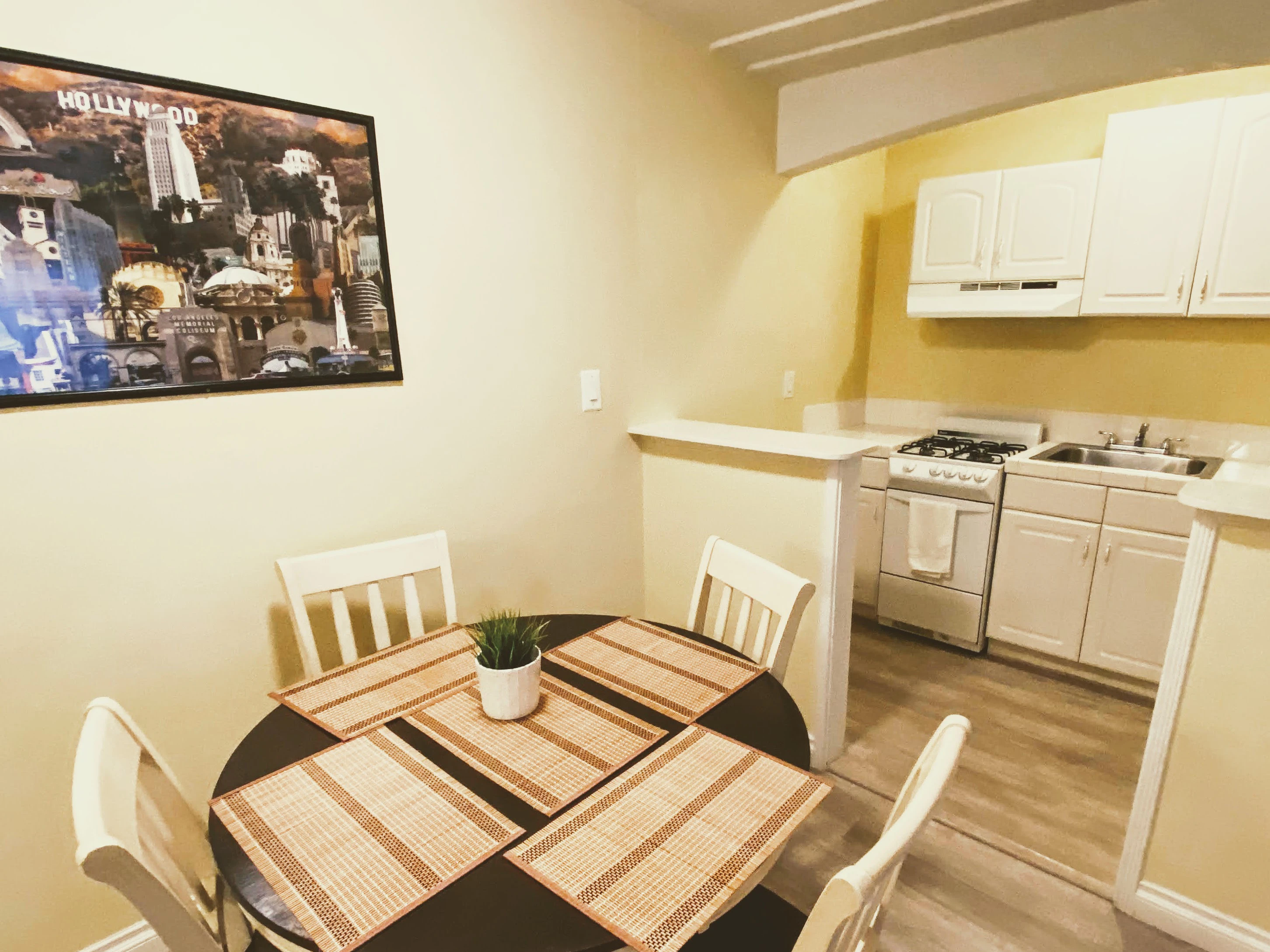 A kitchen with a dining area, featuring a round table with four chairs, a stove, sink, and cabinets.